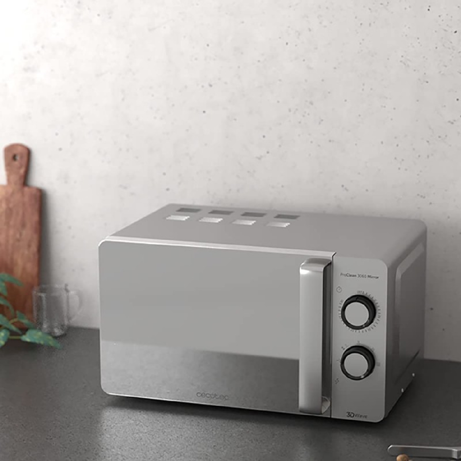Un forno a microonde grigio su un piano di lavoro. Un tagliere e un bicchiere a sinistra. Comandi a destra.