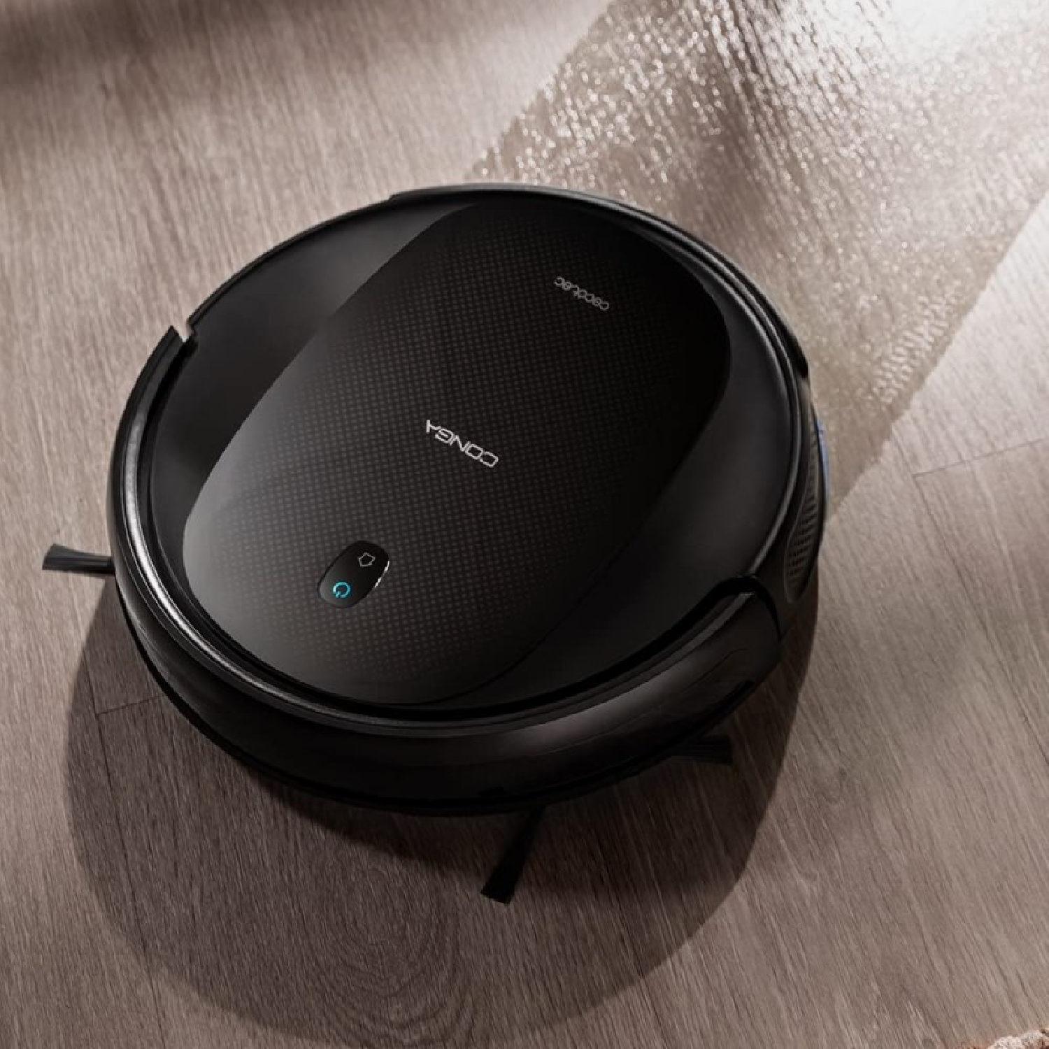Un aspirapolvere robotico nero su un pavimento in legno. È rotondo con il marchio 'CONGA'. Sta pulendo una sezione del pavimento.