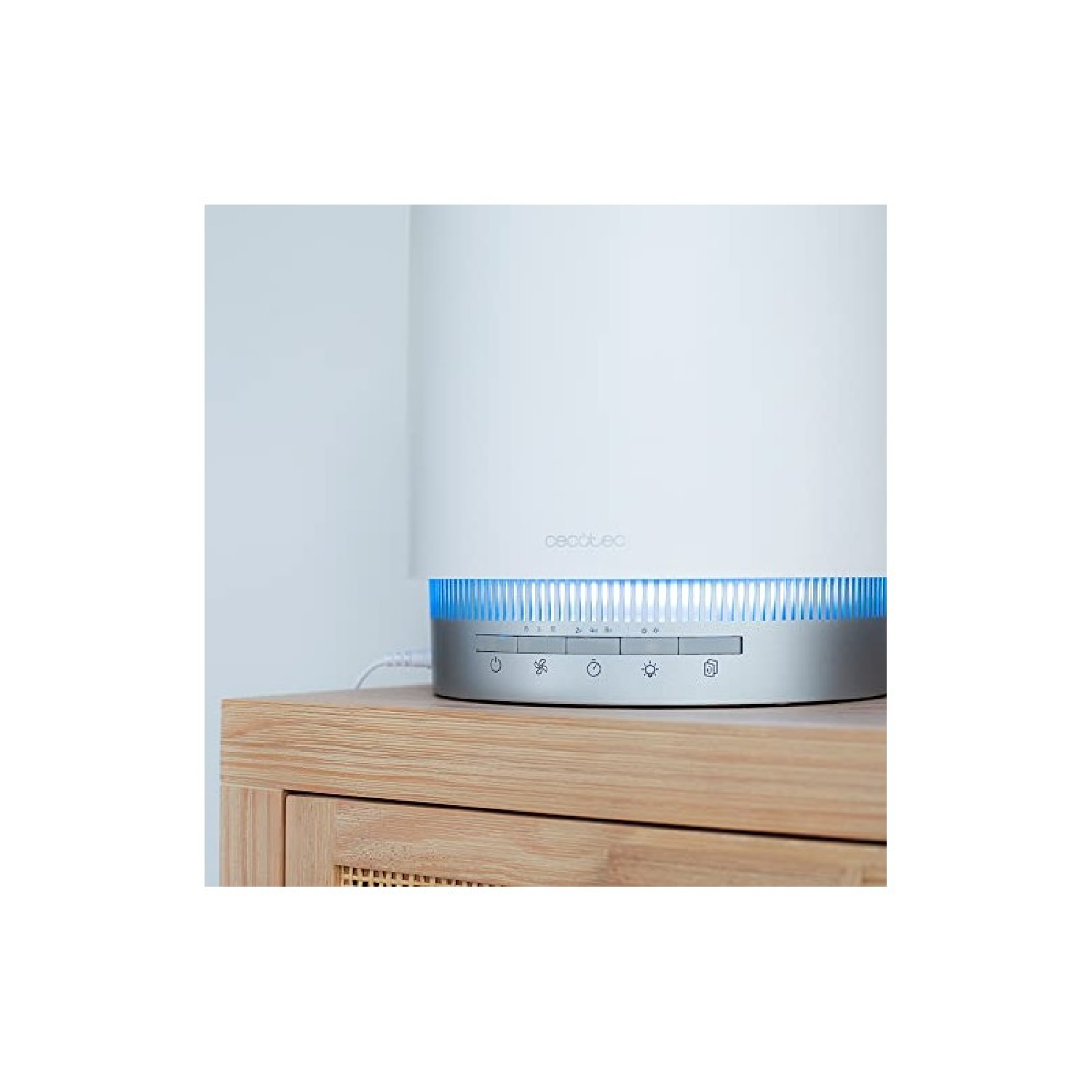 Un purificatore d'aria bianco con base argentata e luci blu, su un mobile in legno, contro un muro bianco.