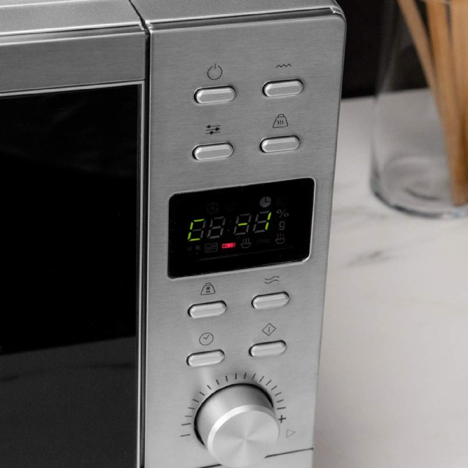 Zbliżenie panelu sterowania kuchenki mikrofalowej. Widoczne przyciski, wyświetlacz cyfrowy z czasem i pokrętło.