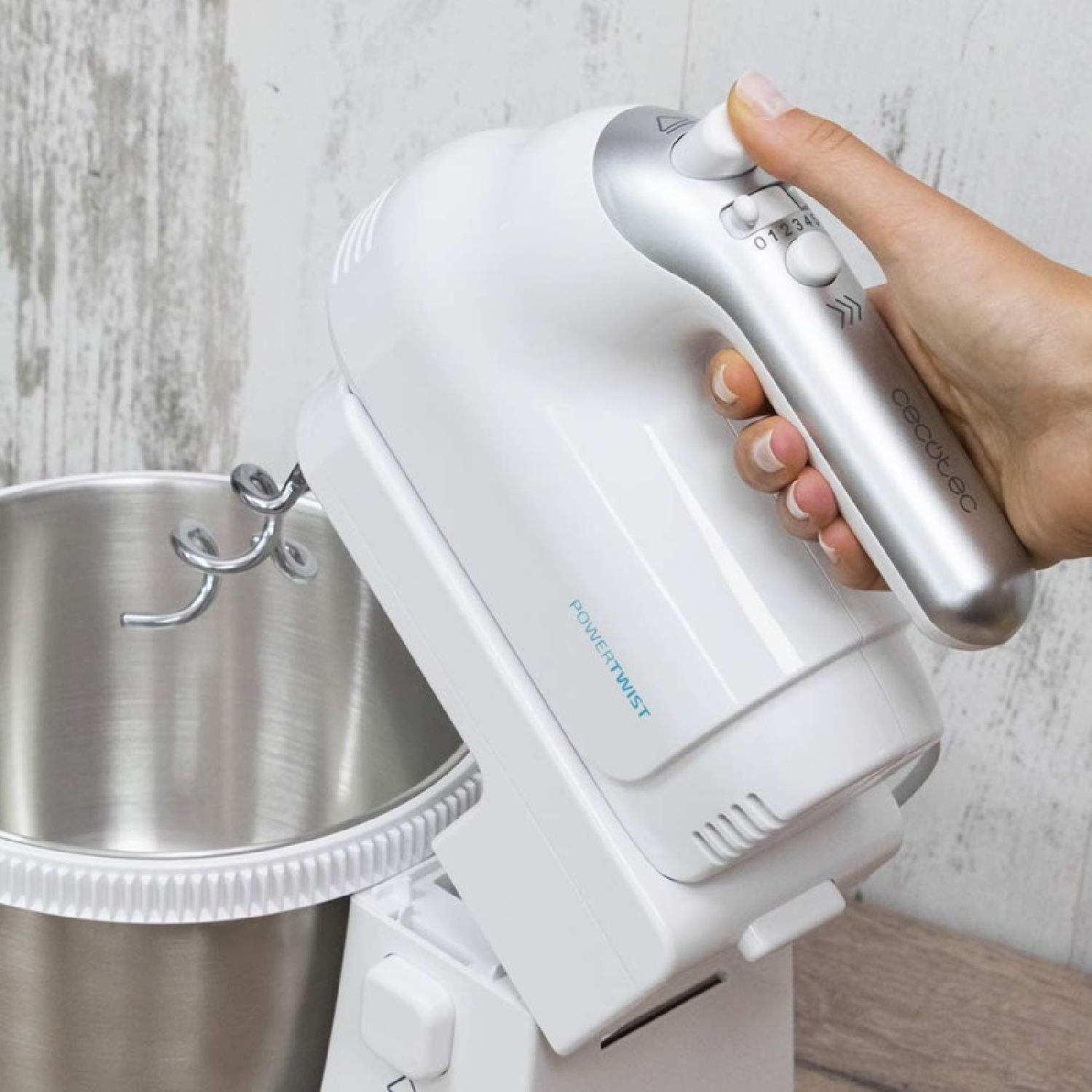 Ein weißer Handmixer mit silbernem Bedienfeld und Edelstahlschüssel wird von einer Hand gehalten. Der Hintergrund ist eine Holzoberfläche.