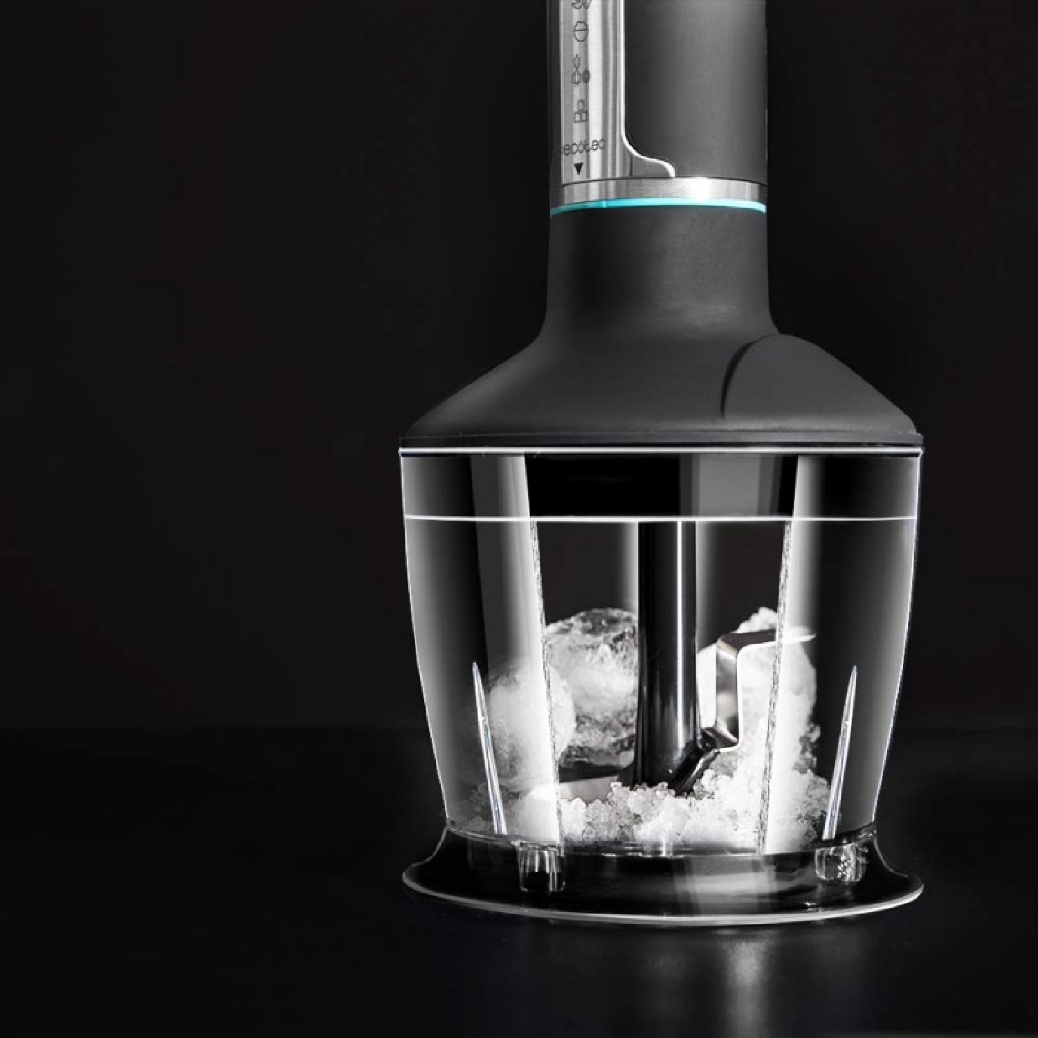 Czarny i srebrny blender ręczny z przezroczystym pojemnikiem wypełnionym lodem. Tło jest ciemne.