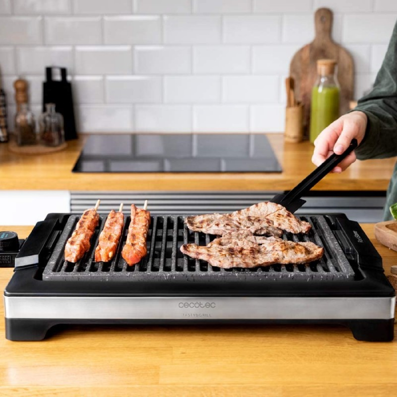 Una griglia con carne è su una superficie di legno. Una persona usa delle pinze per girare la carne. Sfondo cucina.