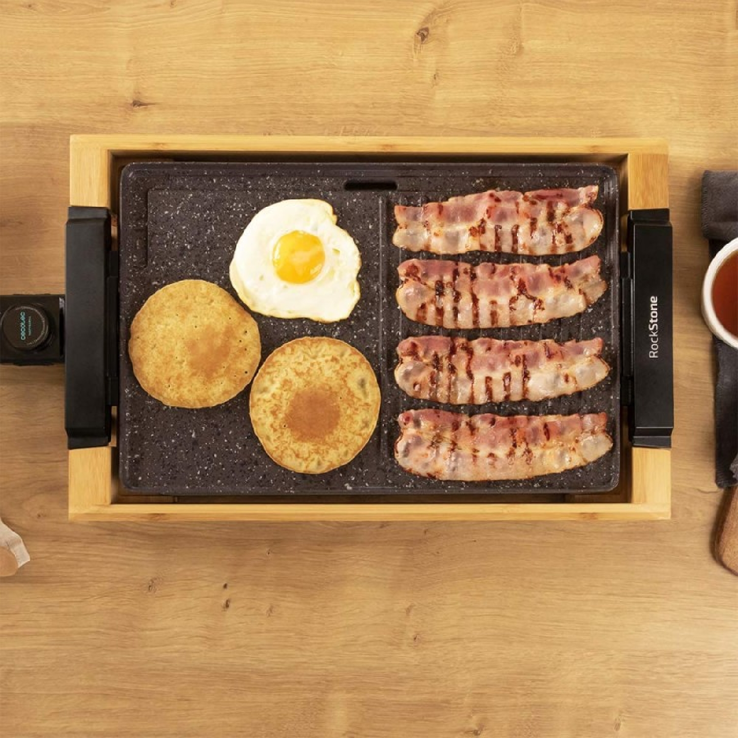 Overzichtsfoto van een ontbijtgriddle met pannenkoeken, ei en spek. De griddle staat op een houten oppervlak.