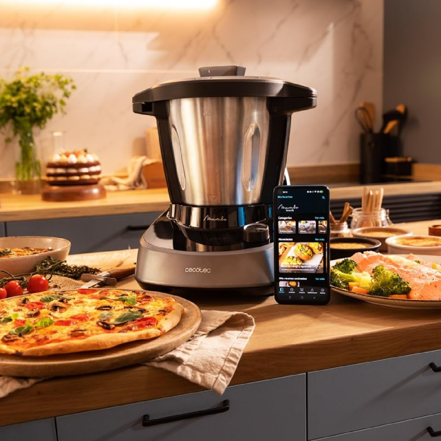 Una scena di cucina con cibo ed elettrodomestici. Un robot da cucina è accanto a un telefono che mostra un'app di ricette. Pizza, pesce e torta sono visibili.