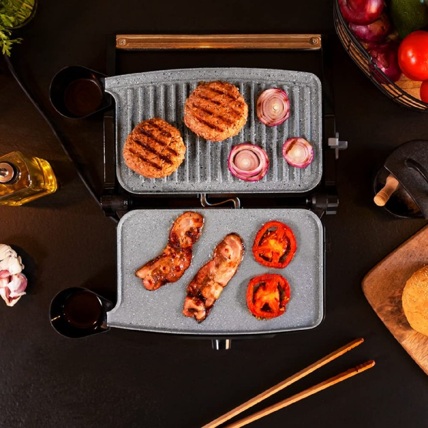 Grill met burgers, spek, tomaten en uien. Ingrediënten op een zwart oppervlak. Mand met groenten en eetstokjes.