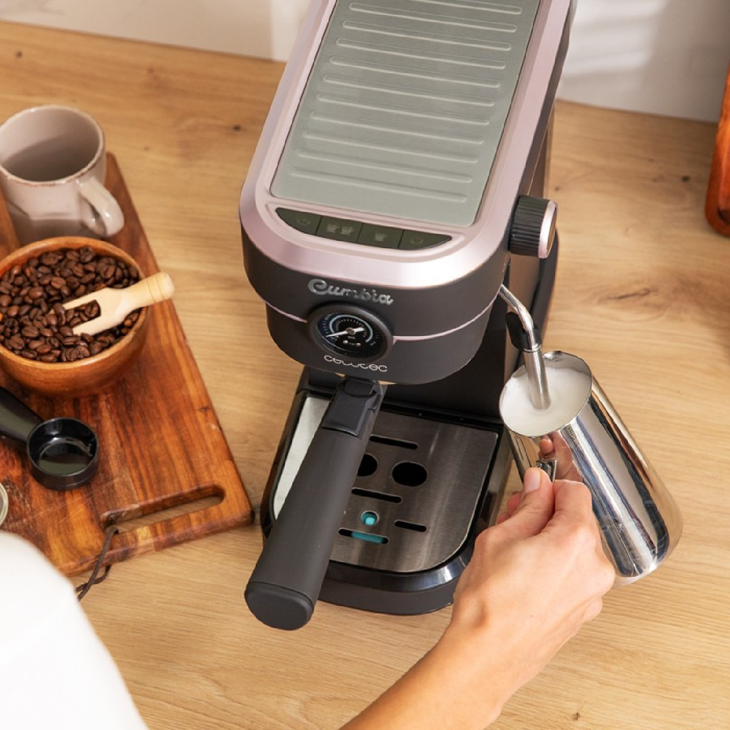 Eine Kaffeemaschine, mit einer Person, die Milch aufschäumt. Kaffeebohnen, eine Tasse und ein Holzbrett links.