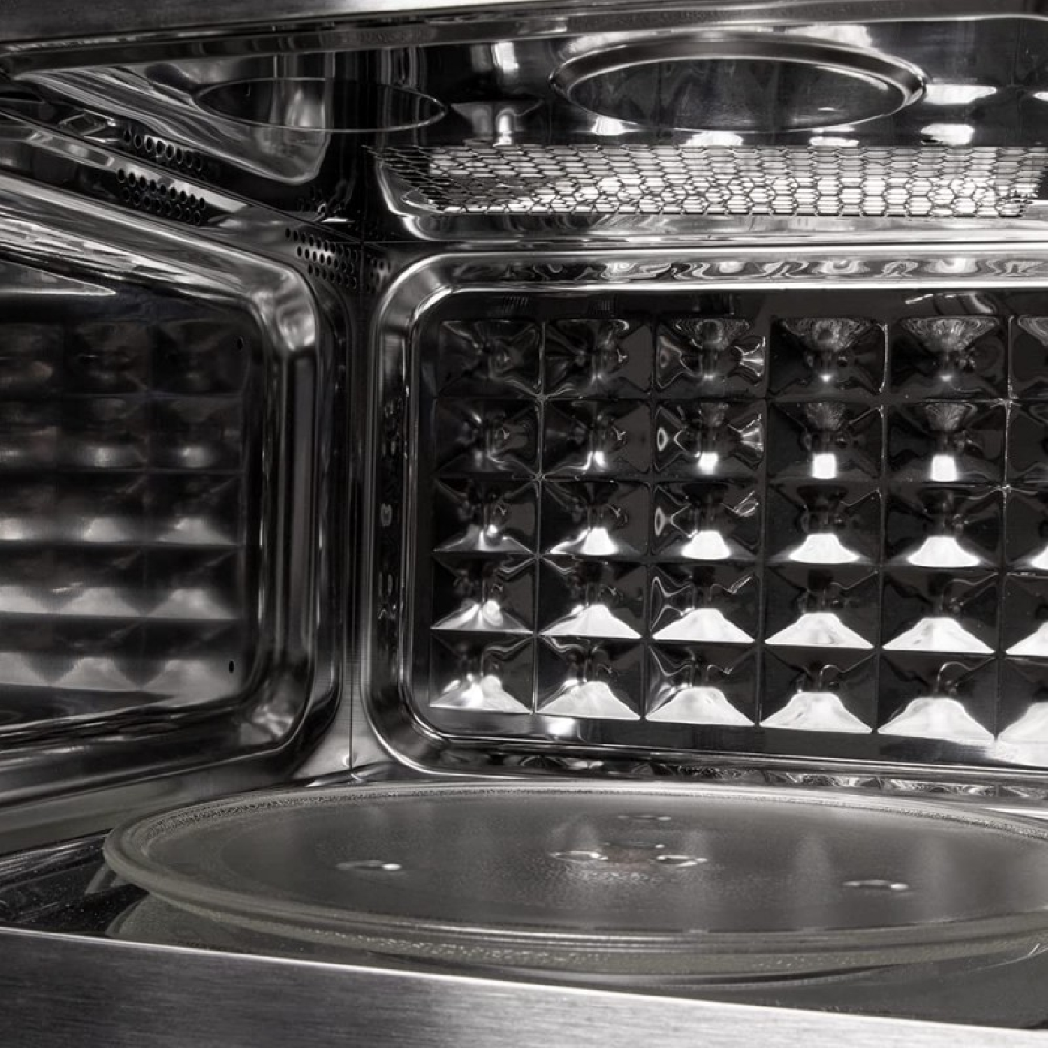 Wnętrze kuchenki mikrofalowej. Szklana płyta znajduje się na dole. Ściany są z błyszczącego metalu. U góry znajduje się metalowa kratka.