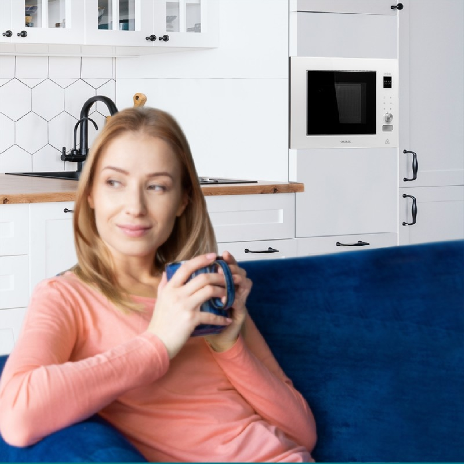 Kobieta z kubkiem na niebieskiej kanapie w kuchni. W tle kuchenka mikrofalowa i szafki.