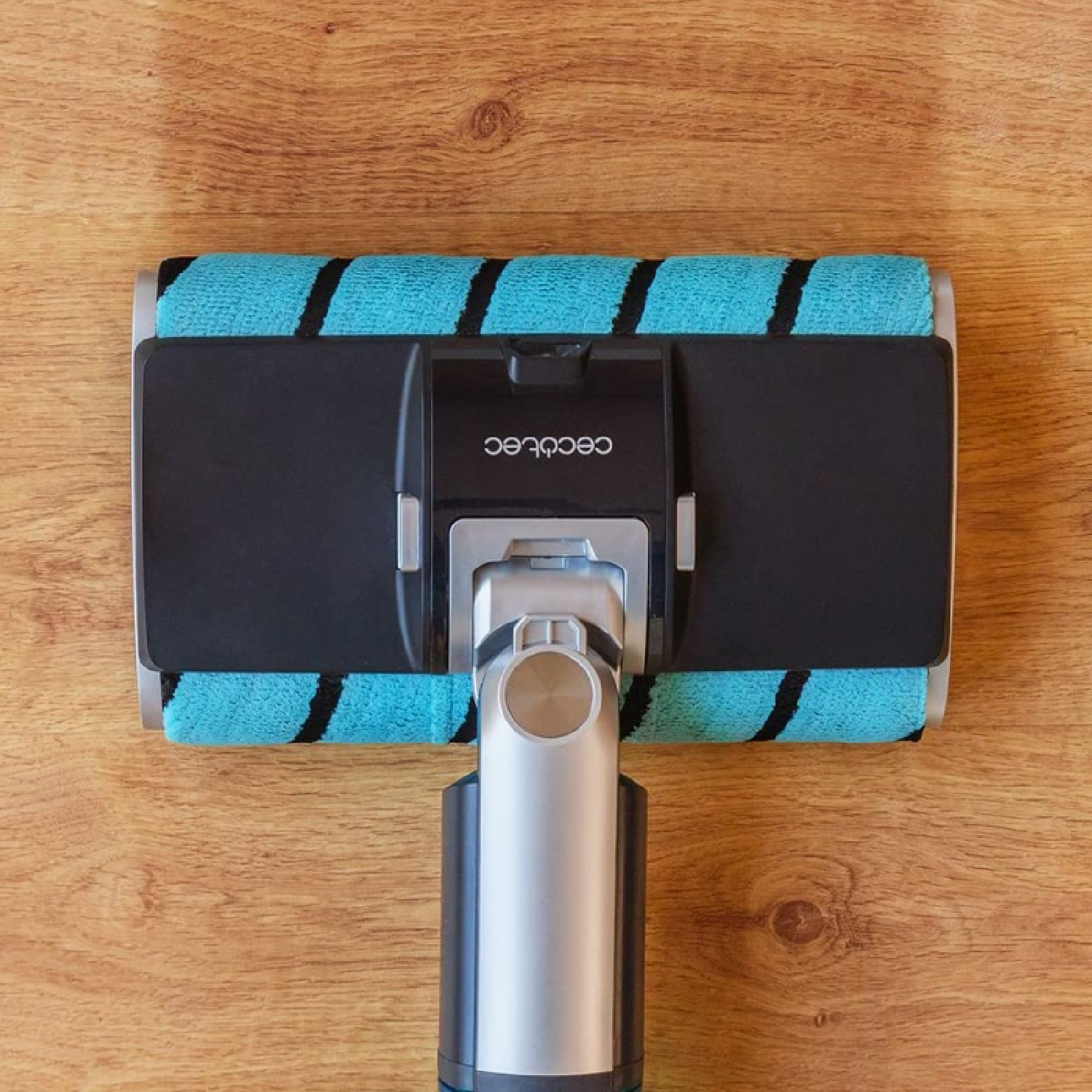 A close-up of a vacuum cleaner head, with a turquoise roller and black stripes, on a wooden surface.