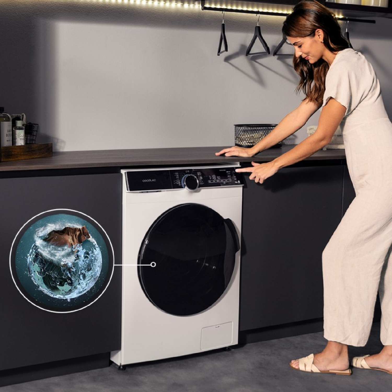 Kobieta w beżowym stroju obsługuje pralkę. Okrągła wstawka pokazuje ubrania wirujące w wodzie. Pralka jest biało-czarna.