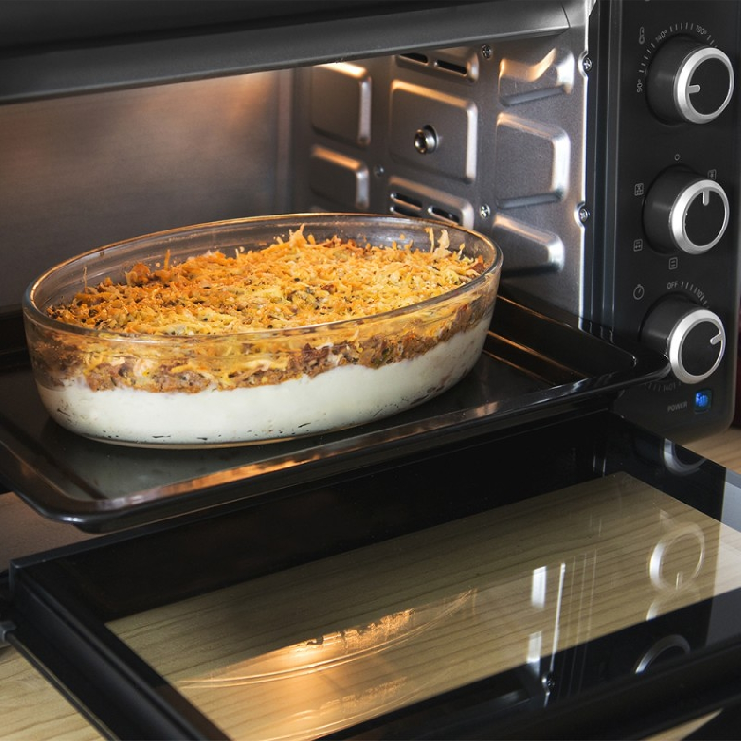 Forno con una pirofila in vetro contenente una casseruola a strati. Lo sportello del forno è aperto. Manopole e comandi sono visibili sul lato del forno.