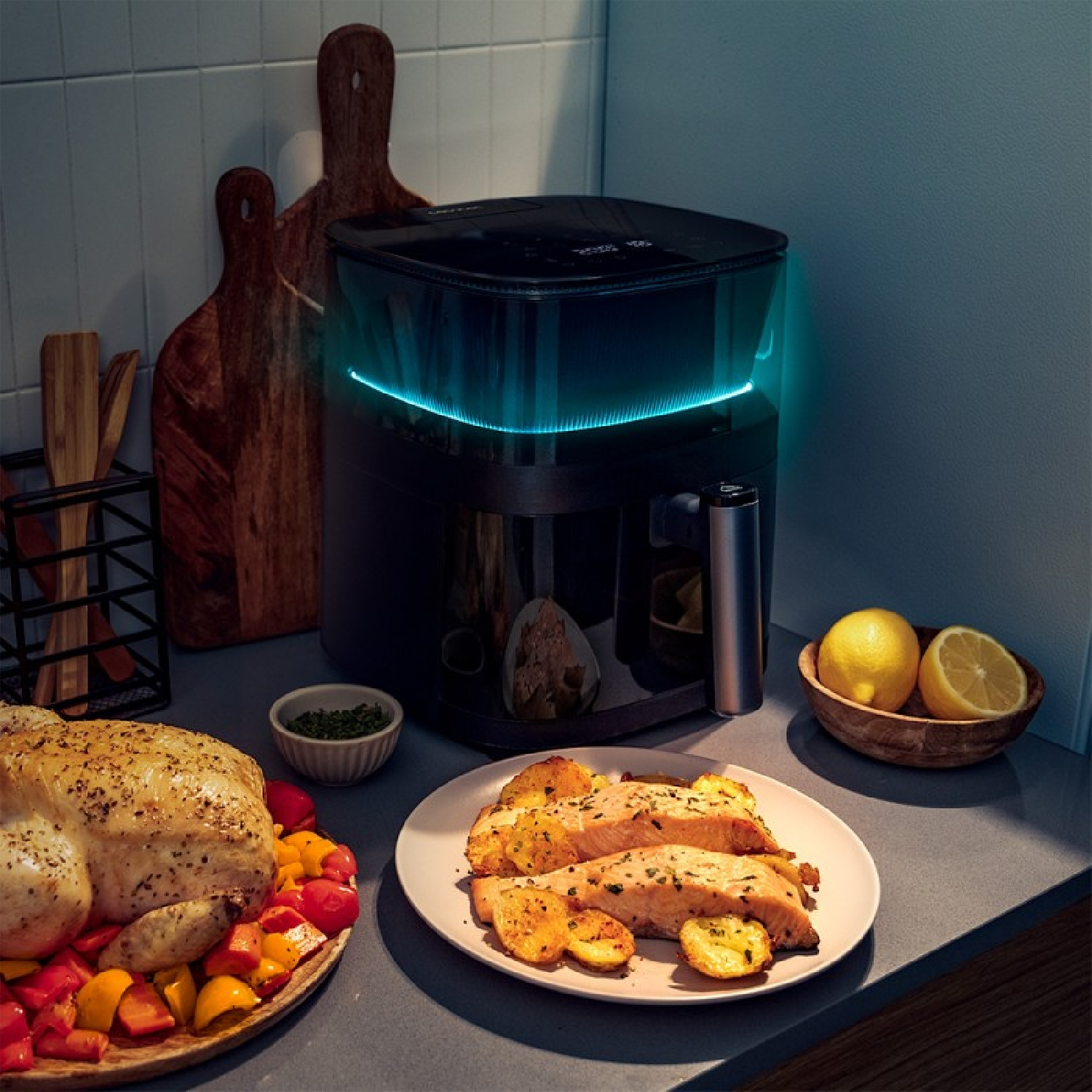Een airfryer met eten. Een gebraden kip, gegrilde zalm en aardappelen, een kom met citroenen en kruiden.