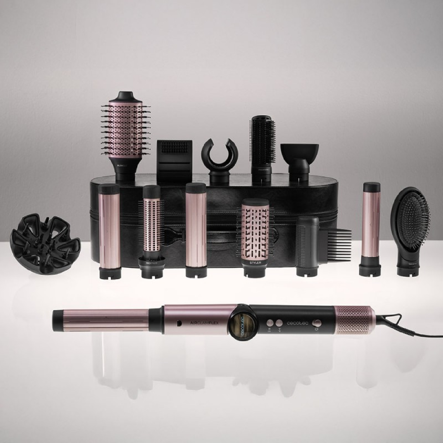 Set per lo styling dei capelli con accessori multipli e un ferro arricciacapelli. I colori nero e oro rosa dominano, disposti su una superficie riflettente.
