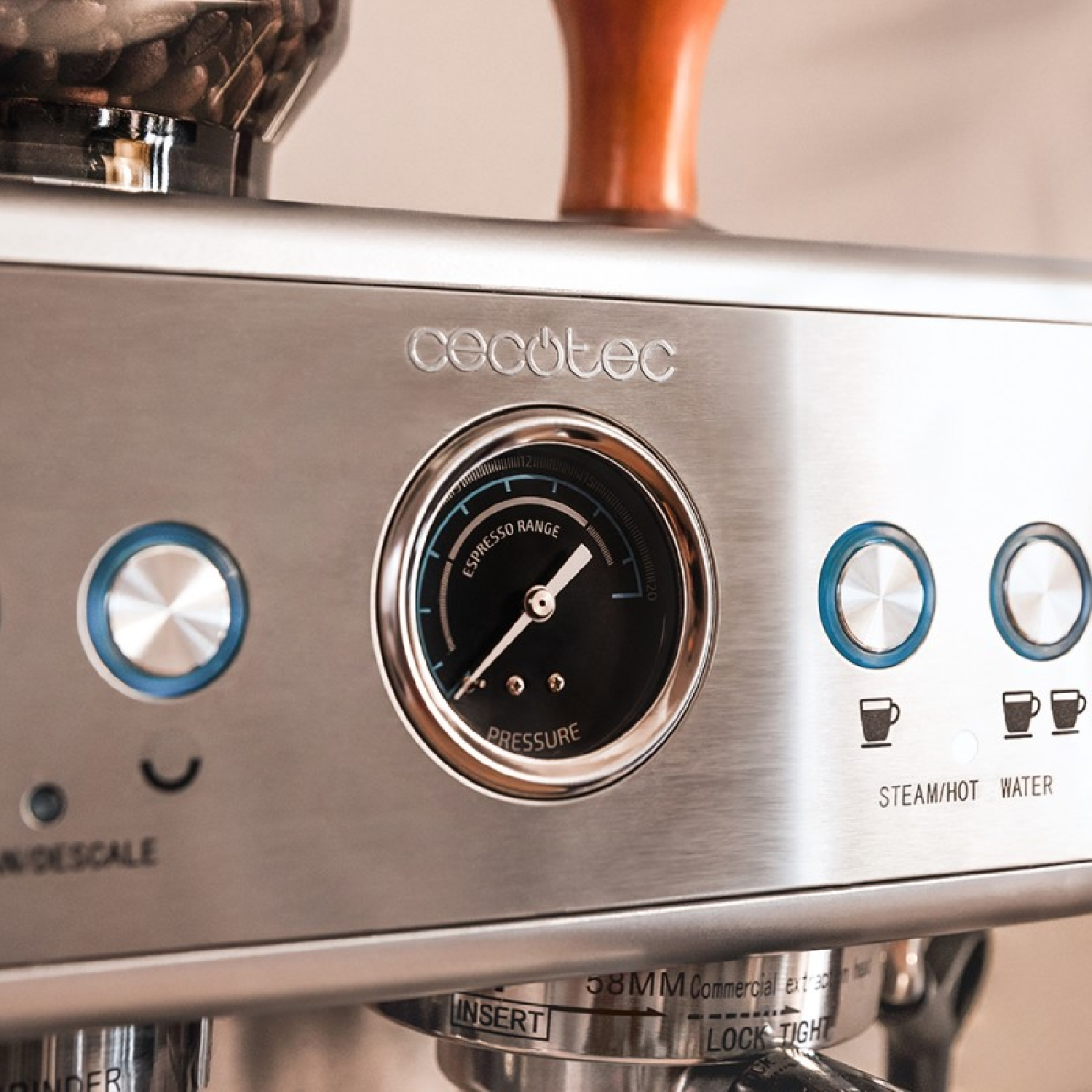 Primer plano de una máquina de espresso plateada. Tiene un manómetro, botones y texto que indica vapor/agua caliente y otras funciones.