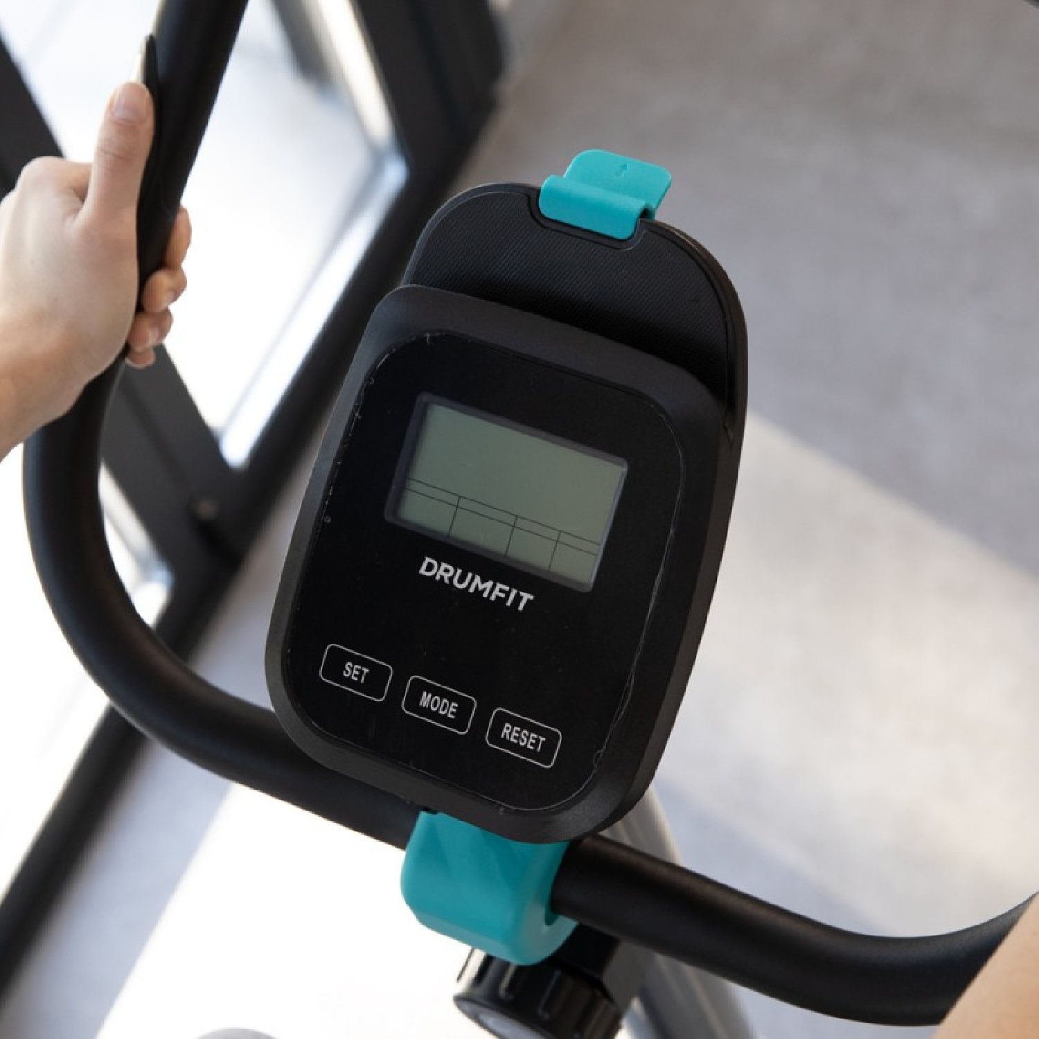 Primo piano del display nero di una cyclette. Il display mostra 'DRUMFIT', pulsanti 'SET', 'MODE' e 'RESET'.