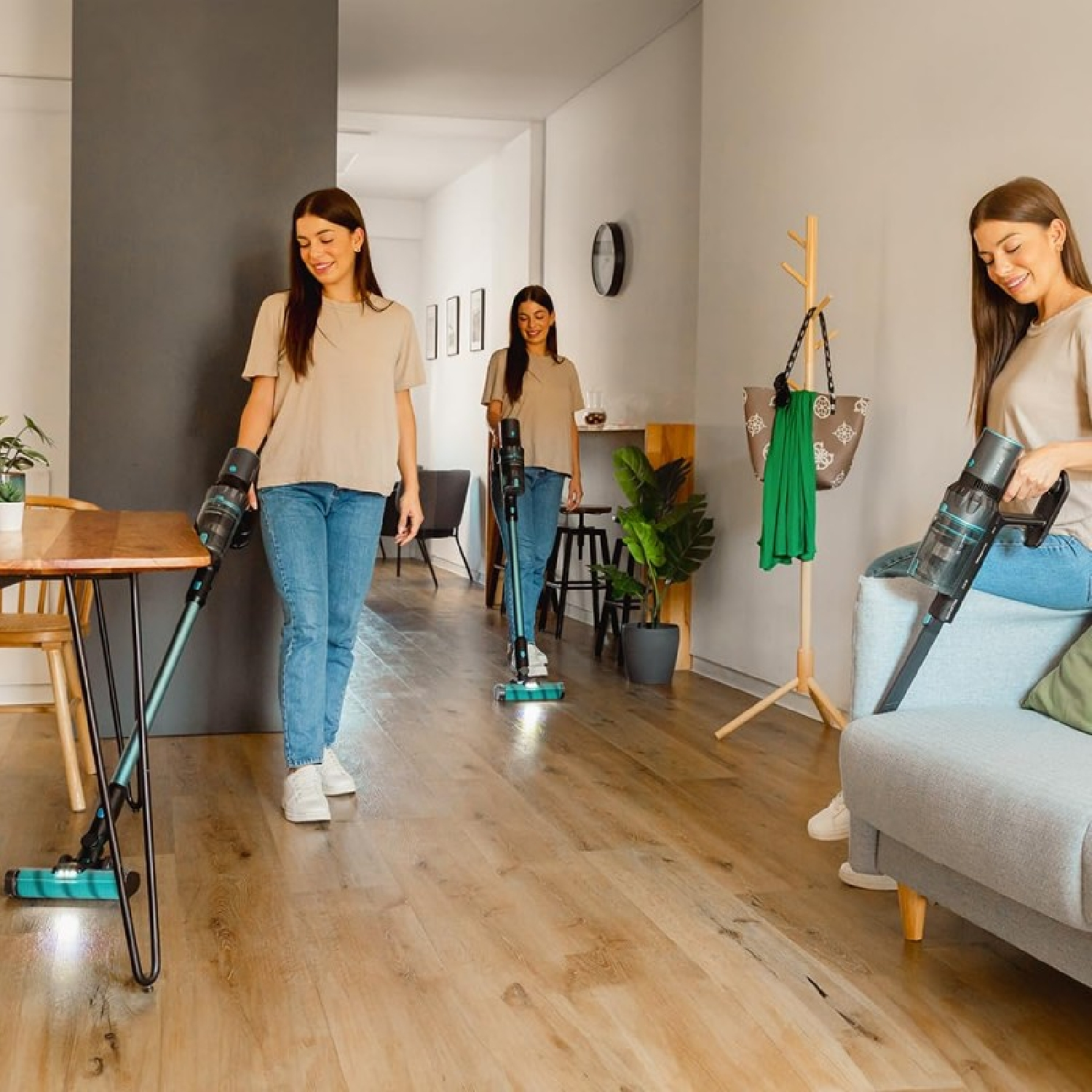 Tre donne aspirano una stanza. Indossano jeans e top beige. Una è seduta su un divano, le altre in piedi. Pavimento in legno.
