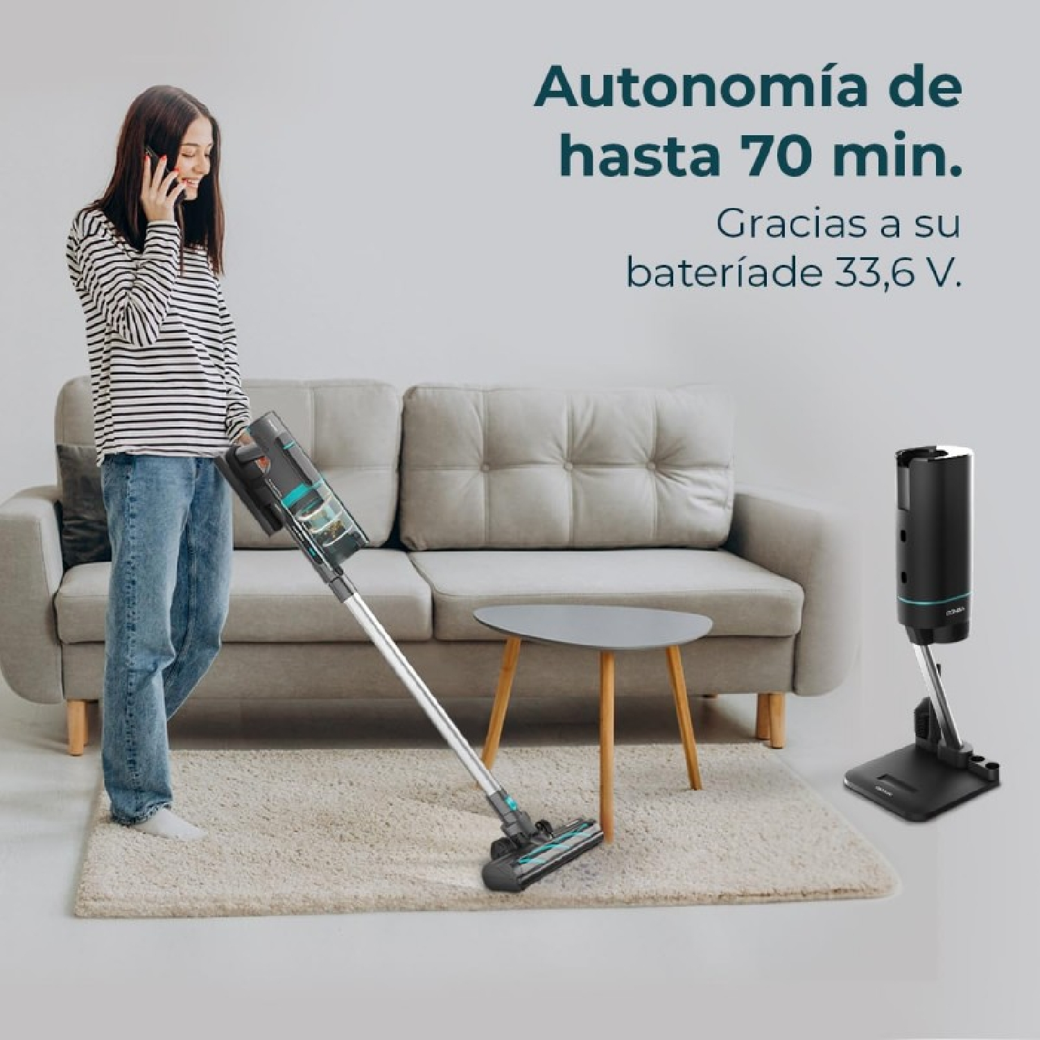 Una donna passa l'aspirapolvere al telefono. Divano, tavolo e base dell'aspirapolvere sullo sfondo. Testo: fino a 70 min.