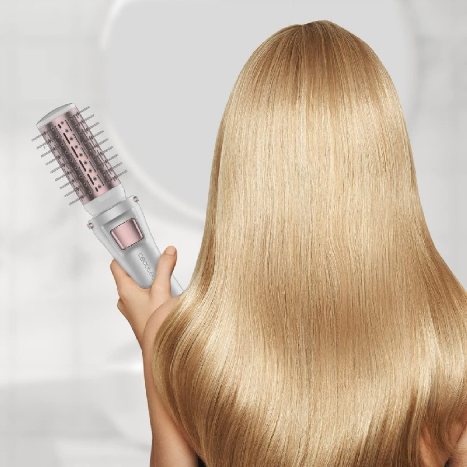 Una persona sostiene un cepillo para el cabello cerca de un cabello largo y rubio. El cepillo es blanco y rosa. El fondo es blanco borroso.