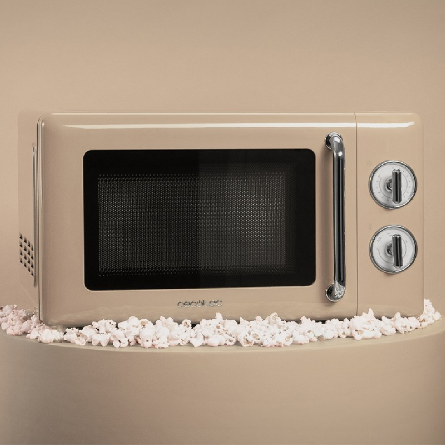 Beżowa kuchenka mikrofalowa z czarnymi drzwiami, chromowanym uchwytem i pokrętłami. Popcorn otacza podstawę. Tło jest jednolicie beżowe.