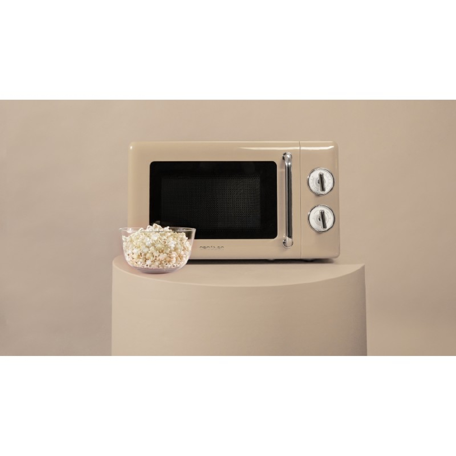 Un forno a microonde beige con una ciotola di vetro di popcorn poggia su un piedistallo beige. Il microonde ha due quadranti e una maniglia.