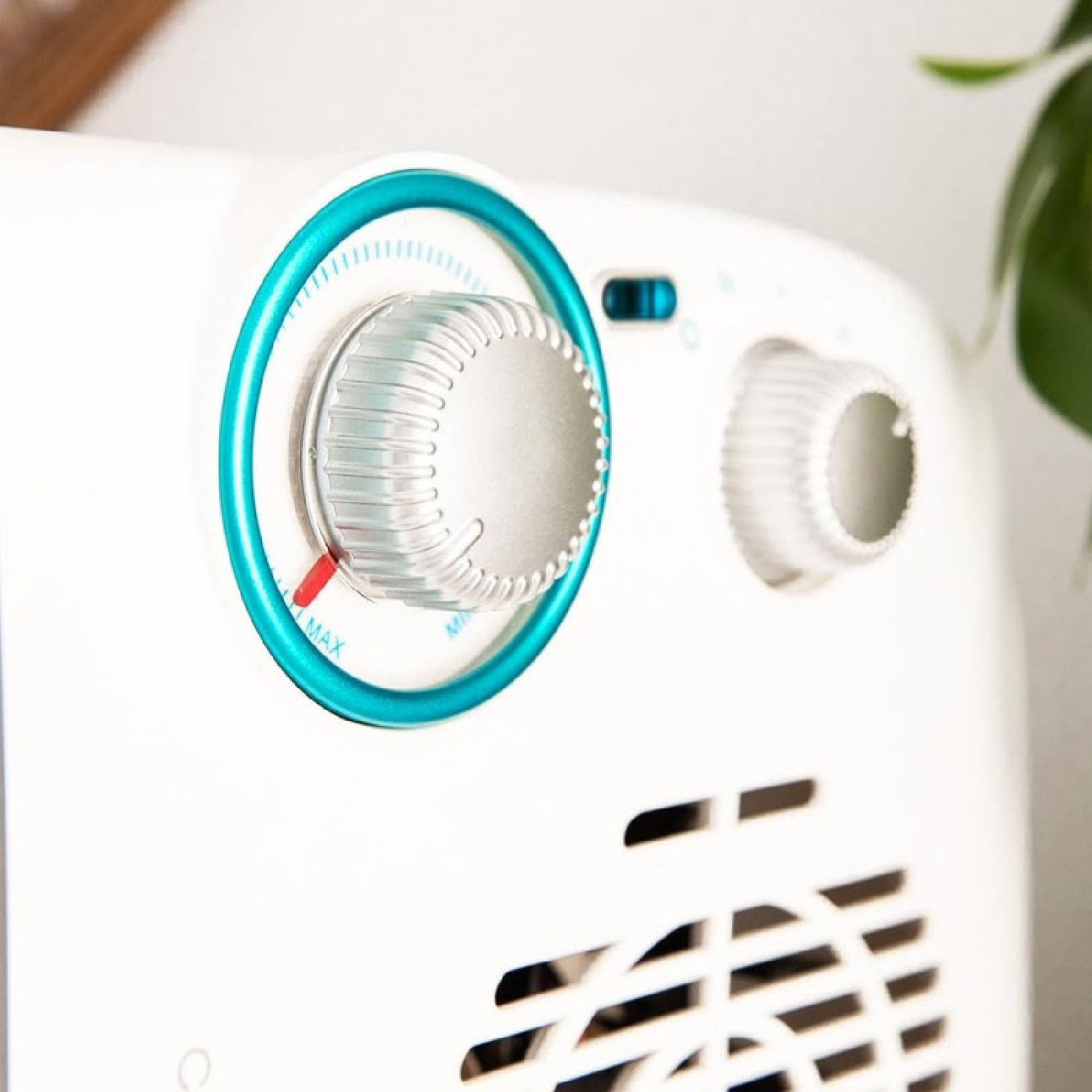 Primo piano di un elettrodomestico bianco con due manopole. La manopola sinistra ha un anello blu e un indicatore rosso. È visibile una griglia di ventilazione.