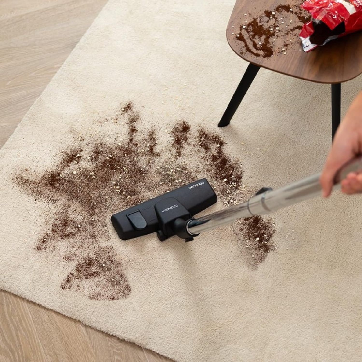 Een stofzuiger maakt een beige tapijt schoon dat bevlekt is met bruin poeder. Een tafel met gemorste poeder en een zak op de achtergrond.