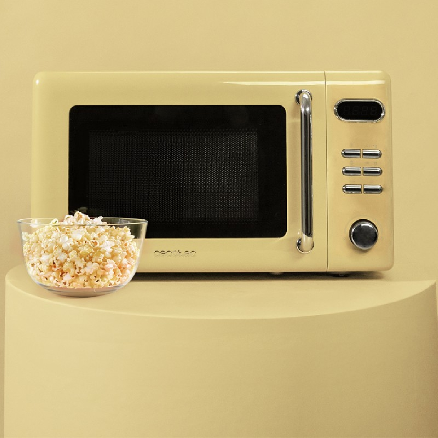 Kremowy kuchenka mikrofalowa i szklana miska z popcornem stoją na żółtej powierzchni. Kuchenka ma uchwyt i przyciski.