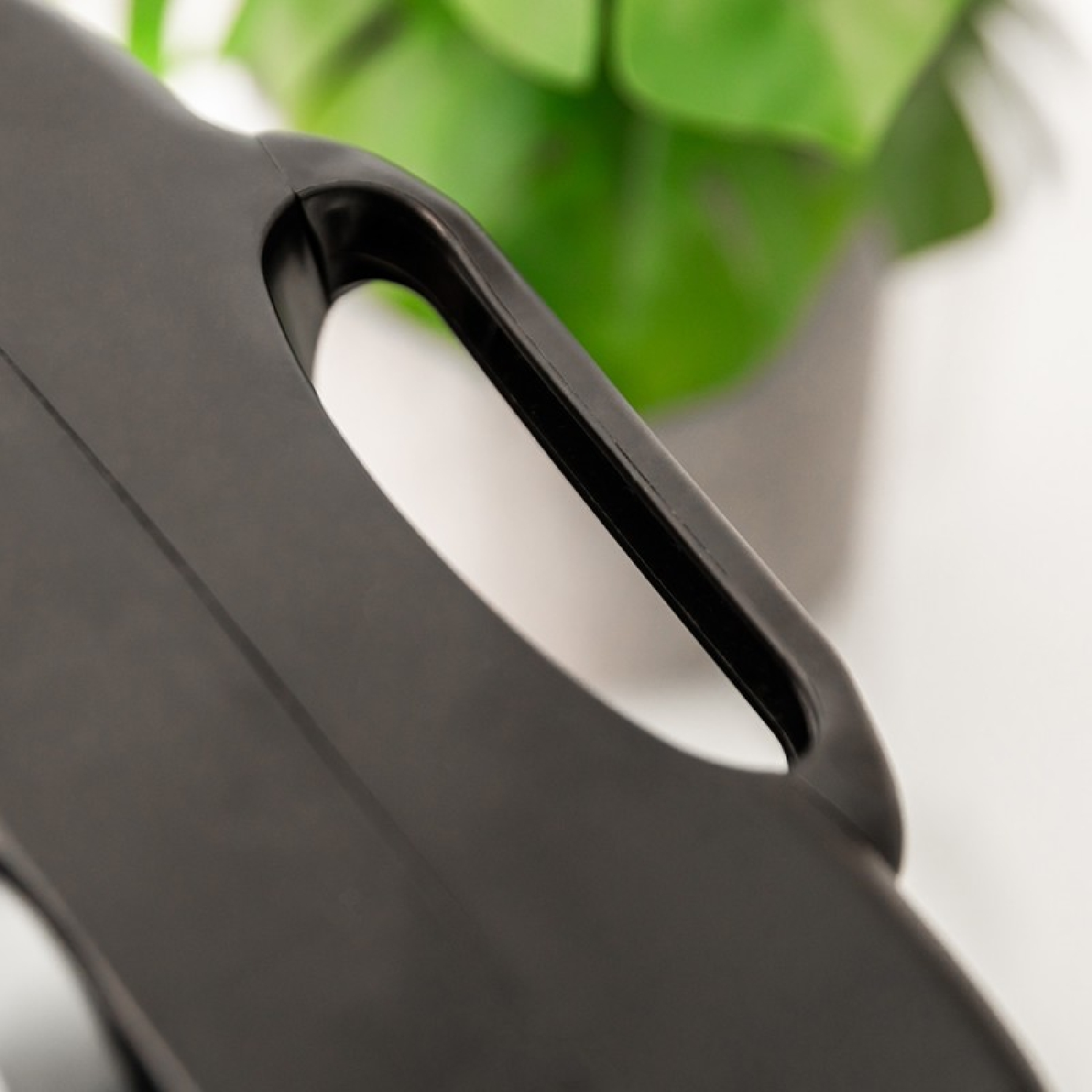 Primo piano di una maniglia in plastica nera dal design curvo. Sullo sfondo sfocato, si vede una pianta verde.
