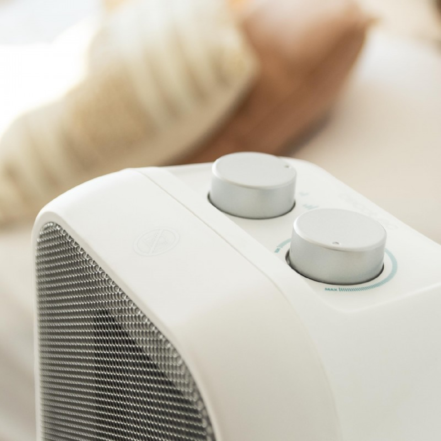 Zbliżenie białego grzejnika ze srebrnymi pokrętłami. Grzejnik ma metalową siatkę i znajduje się w rozmytym pomieszczeniu.