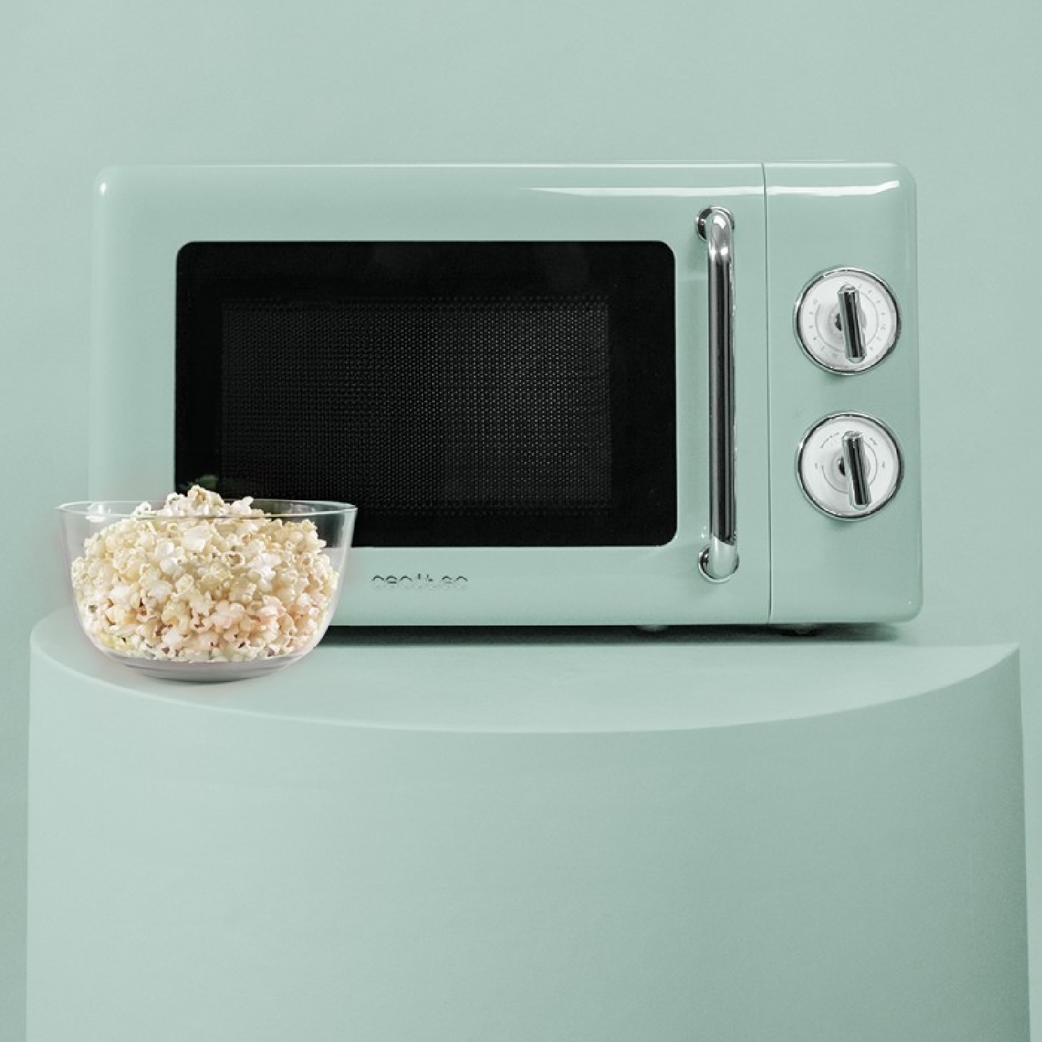 Miętowa kuchenka mikrofalowa obok miski popcornu na miętowym stojaku. Tło jest również miętowe.