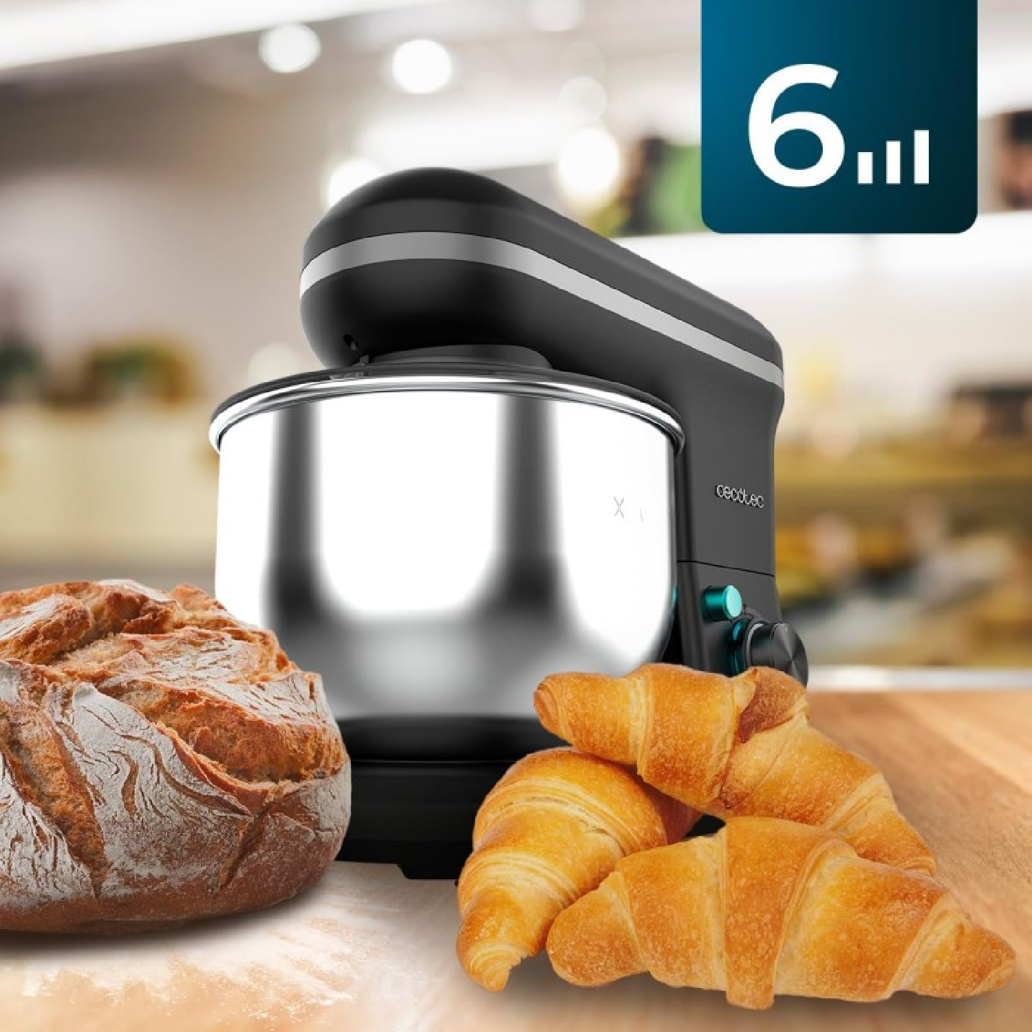 Un mixer nero con ciotola in acciaio inox, una pagnotta e croissant su una superficie di legno.