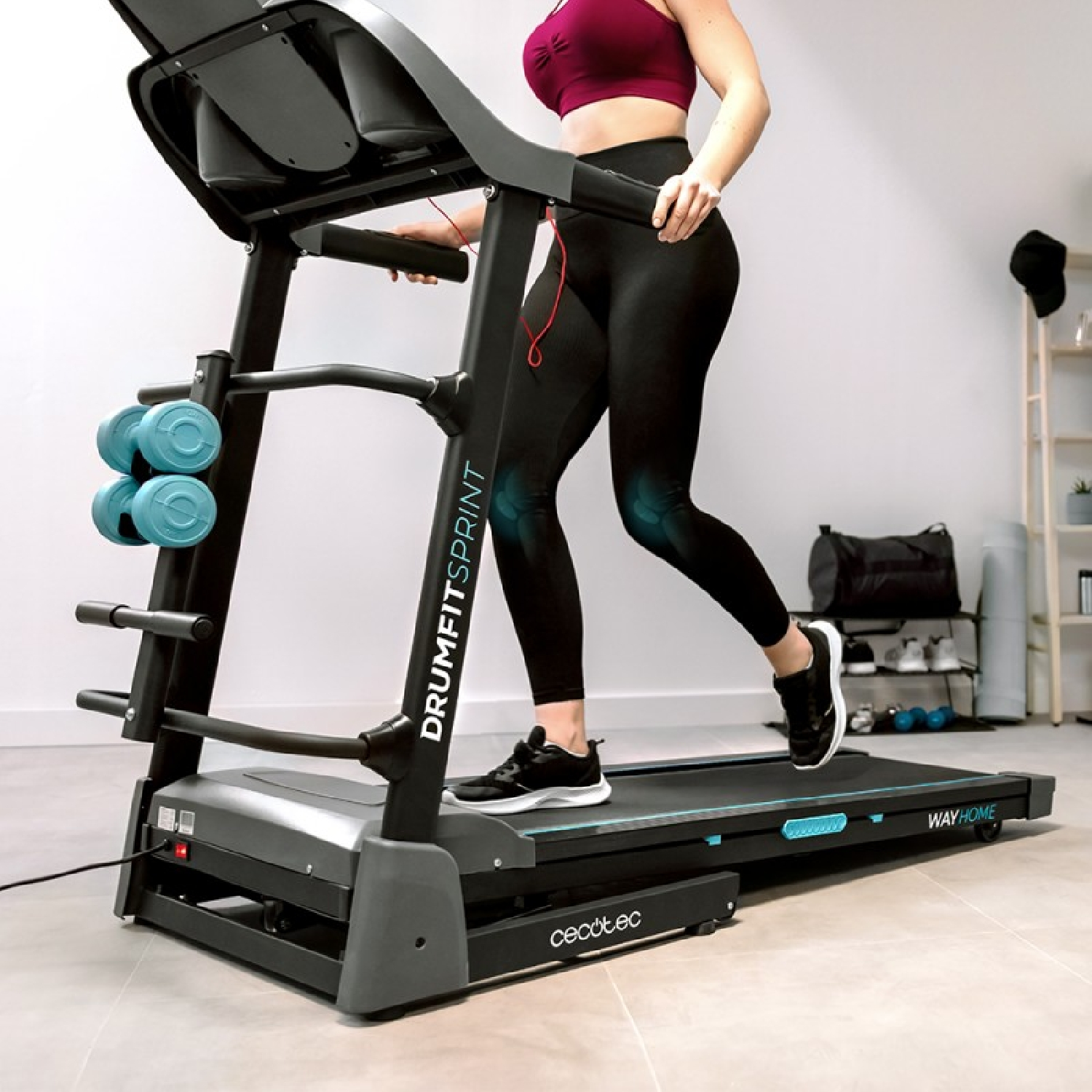 Una mujer corre en una cinta de correr. Lleva leggings negros y un top rojo. La cinta de correr está en un gimnasio en casa.