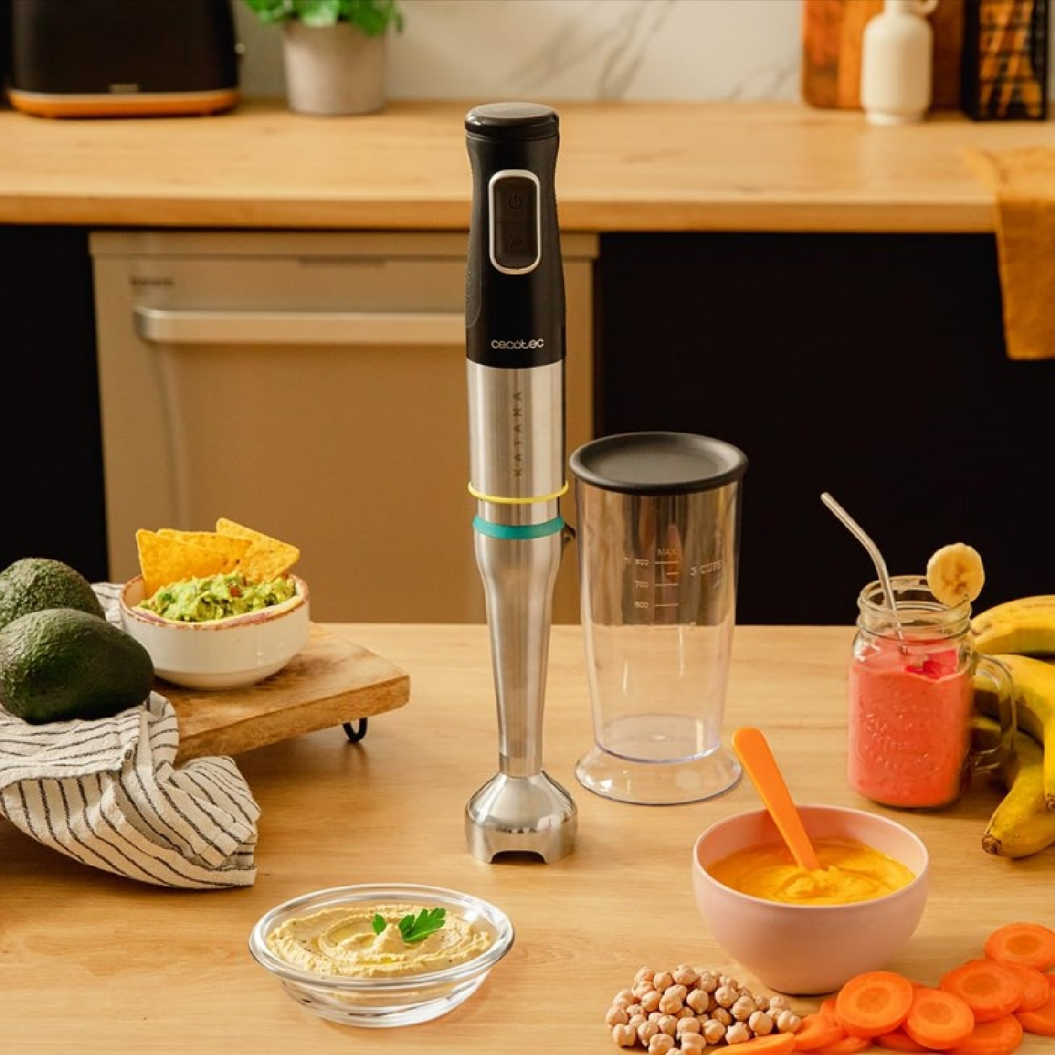 Scena kuchenna z blenderem, koktajlem i warzywami. Obecny jest również hummus, guacamole i marchewka, co sugeruje przygotowywanie posiłków.