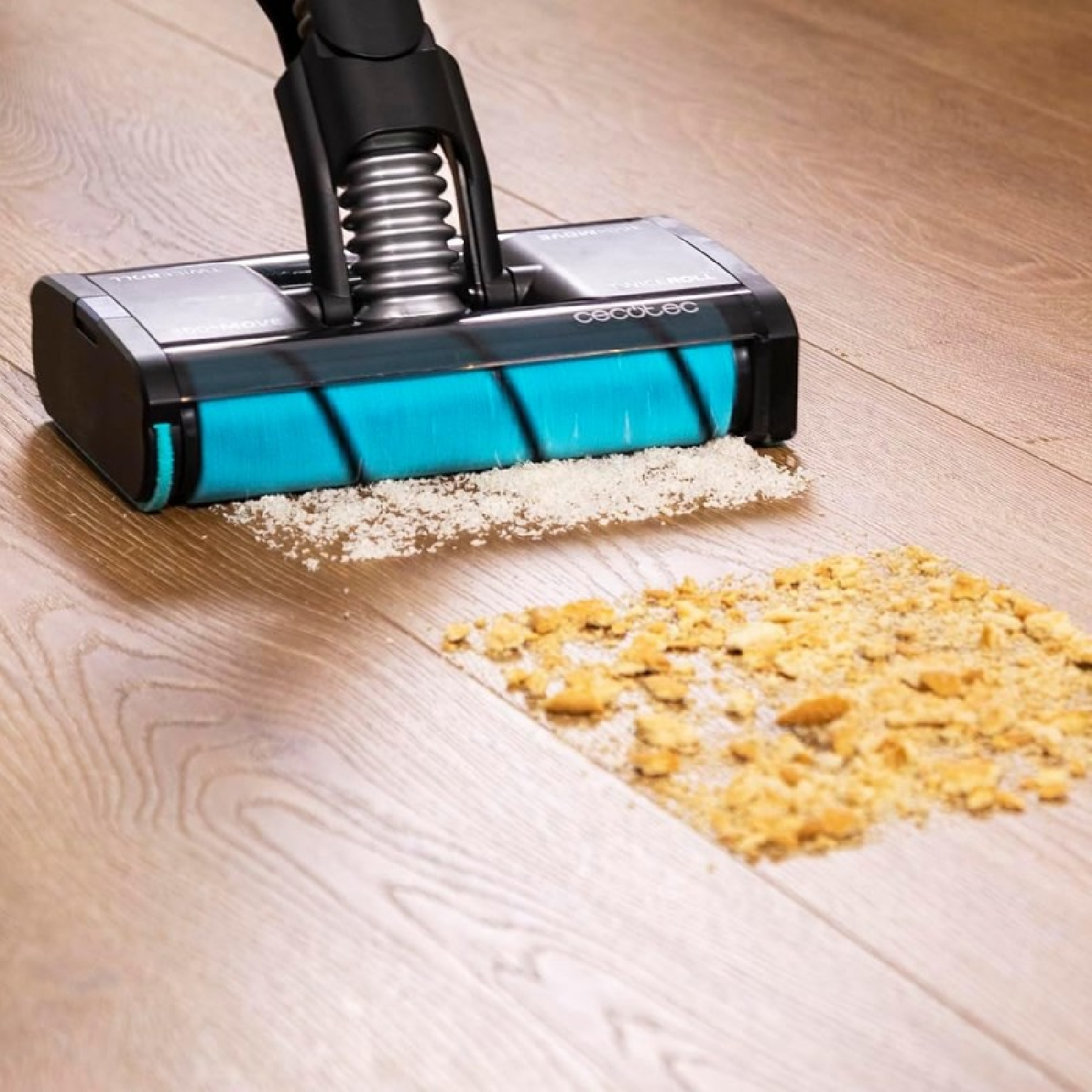 Un aspirapolvere con rullo blu pulisce le briciole da un pavimento in legno. Le briciole sono bianche e gialle.