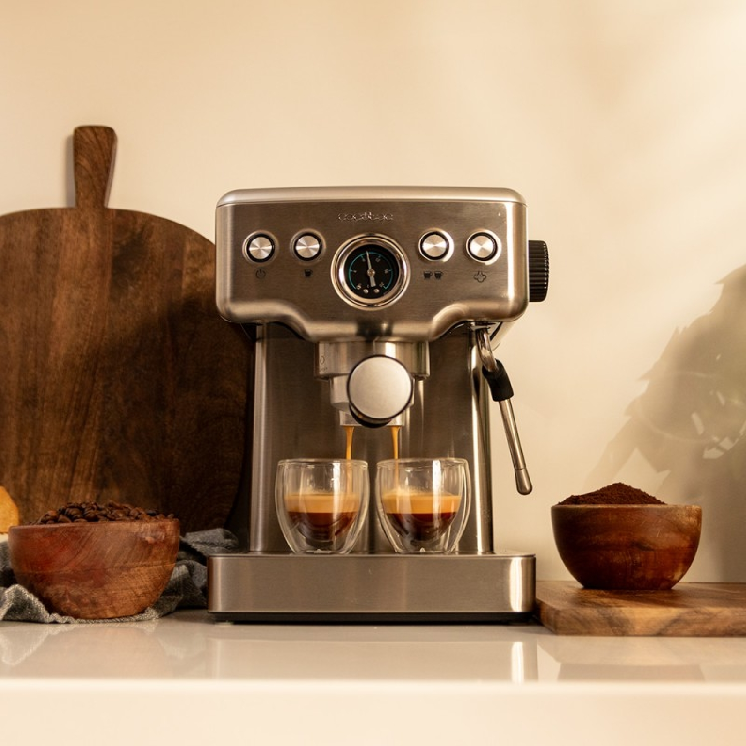 Een koffiemachine zet espresso in twee heldere glazen. Er staan bakjes met koffiebonen en gemalen koffie in de buurt.