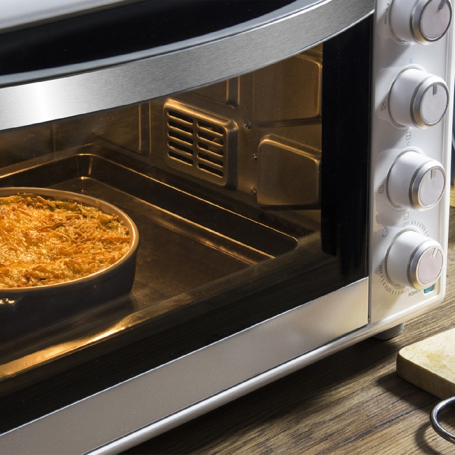 Un forno con un piatto all'interno. È in cottura. Il forno è argento e bianco. Il piatto è rotondo e contiene un pasto cotto.