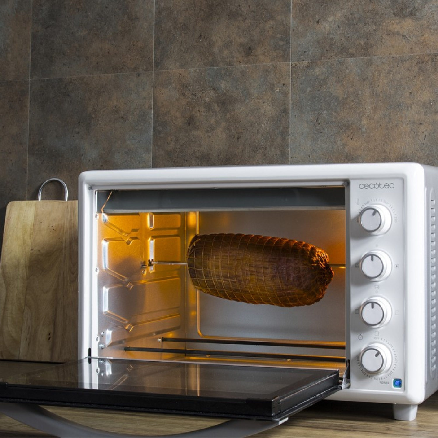 Un forno bianco con carne arrosto all'interno. La porta del forno è aperta. Un tagliere di legno è a sinistra.