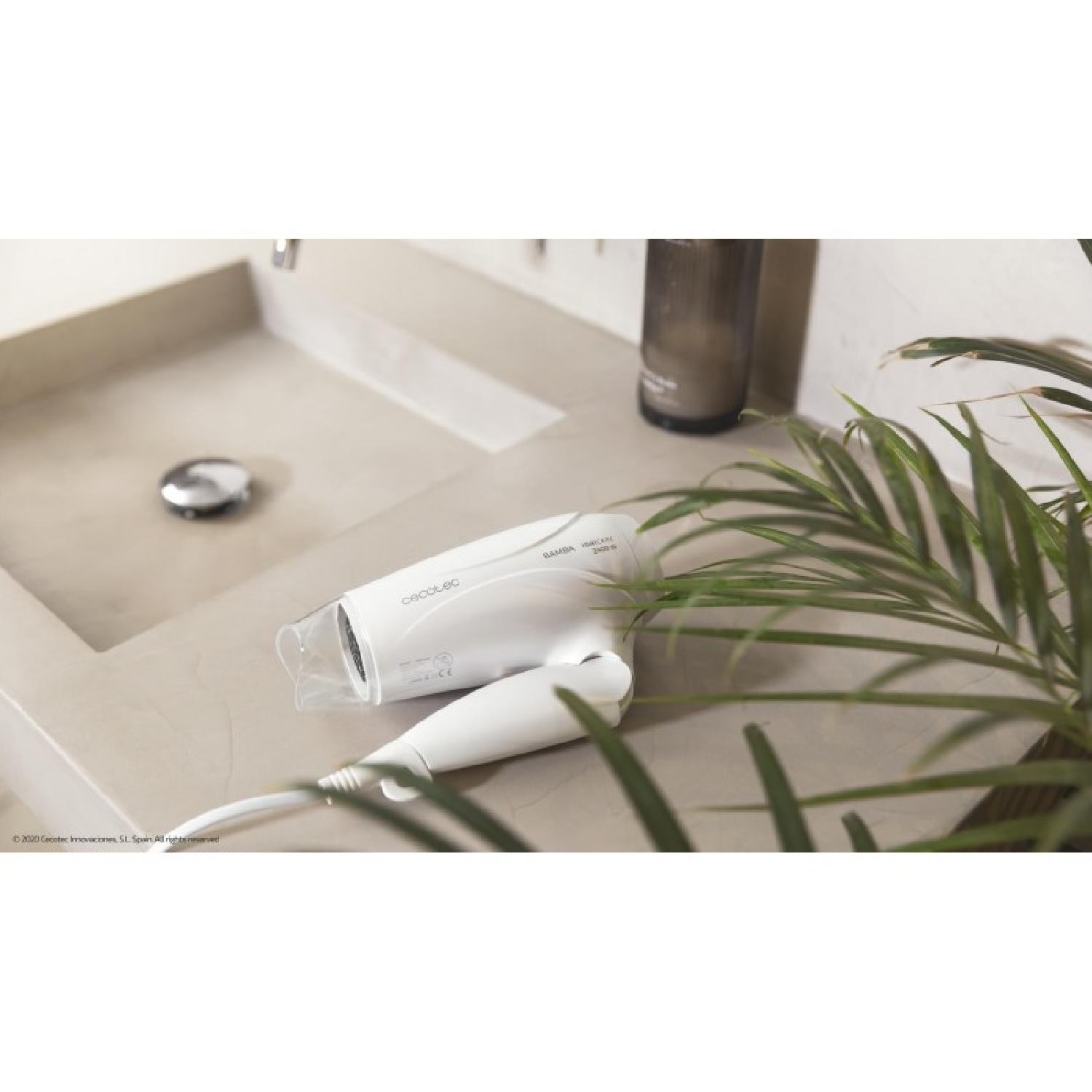 Un asciugacapelli bianco su un ripiano del bagno, con un lavandino e una pianta verde sullo sfondo.