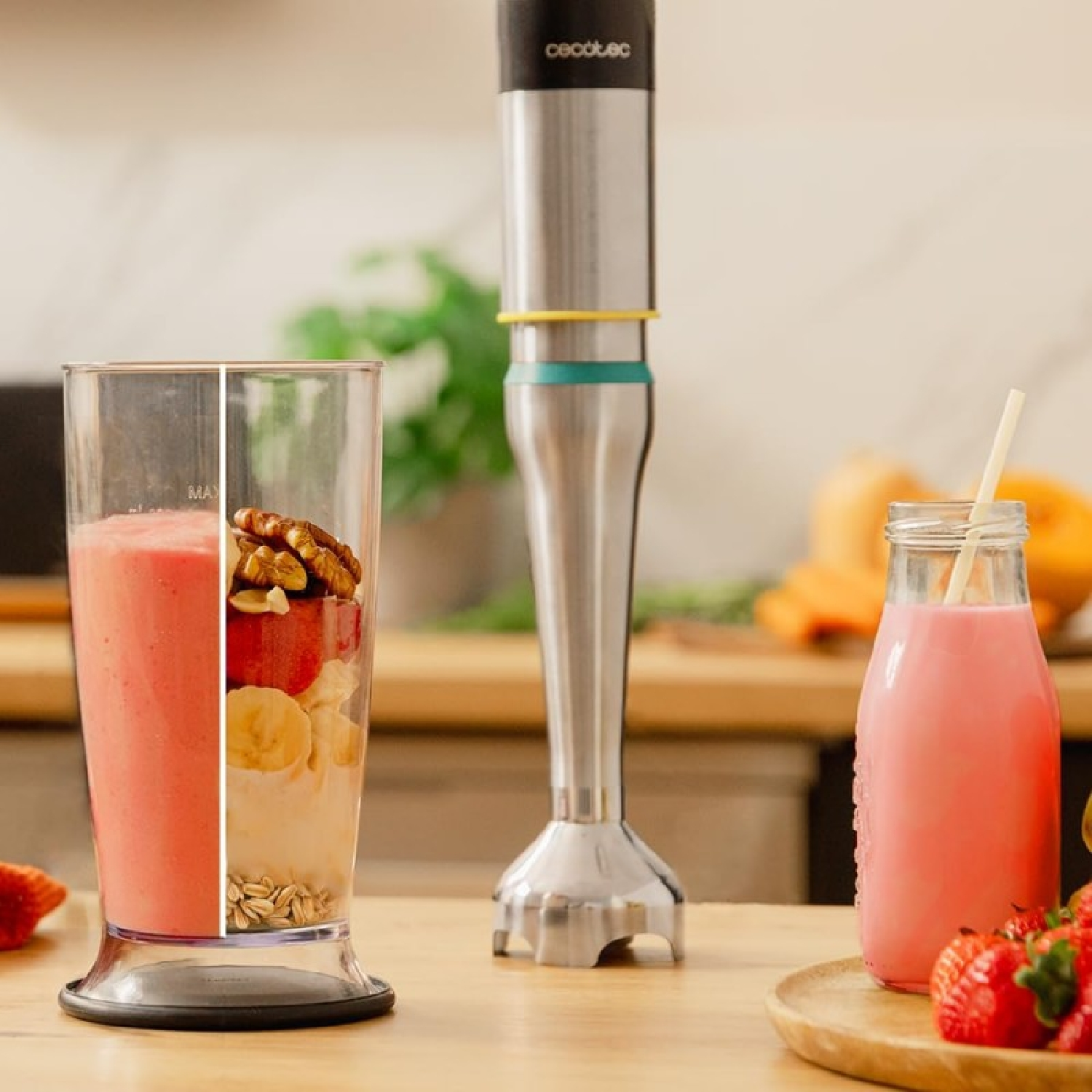 Blender stoi obok szklanki ze smoothie i składnikami. Z przodu butelka smoothie i truskawki.