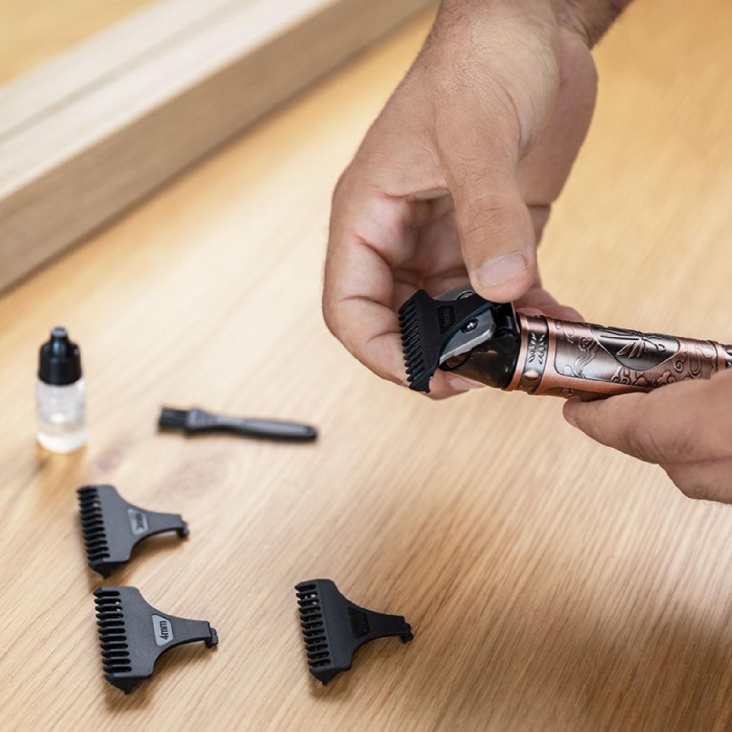 Una mano tiene un trimmer color rame, con diverse protezioni nere e una bottiglia su una superficie di legno.
