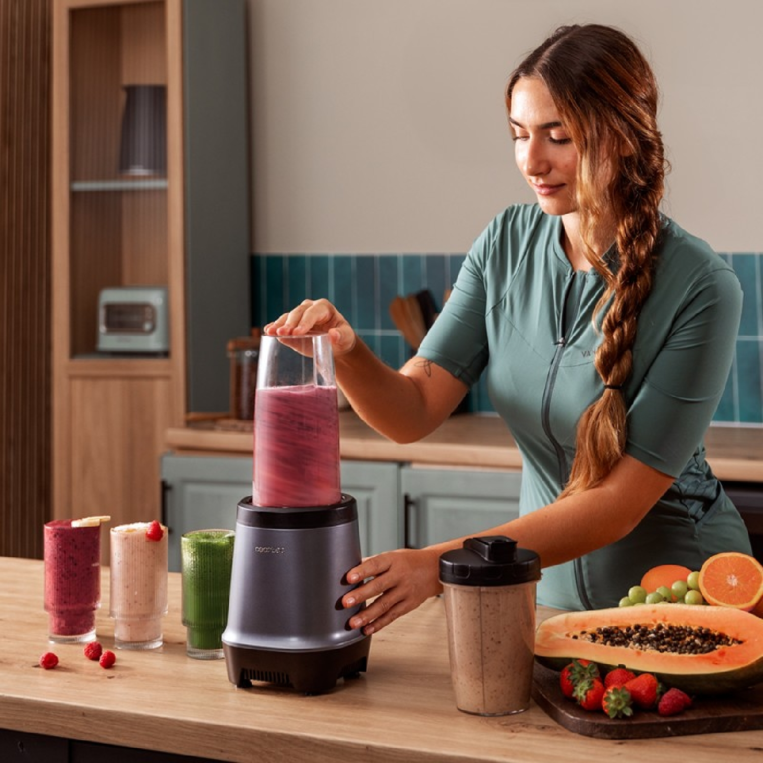 Mujer haciendo un batido con una licuadora. Frutas como papaya, fresas y naranjas están en la encimera.