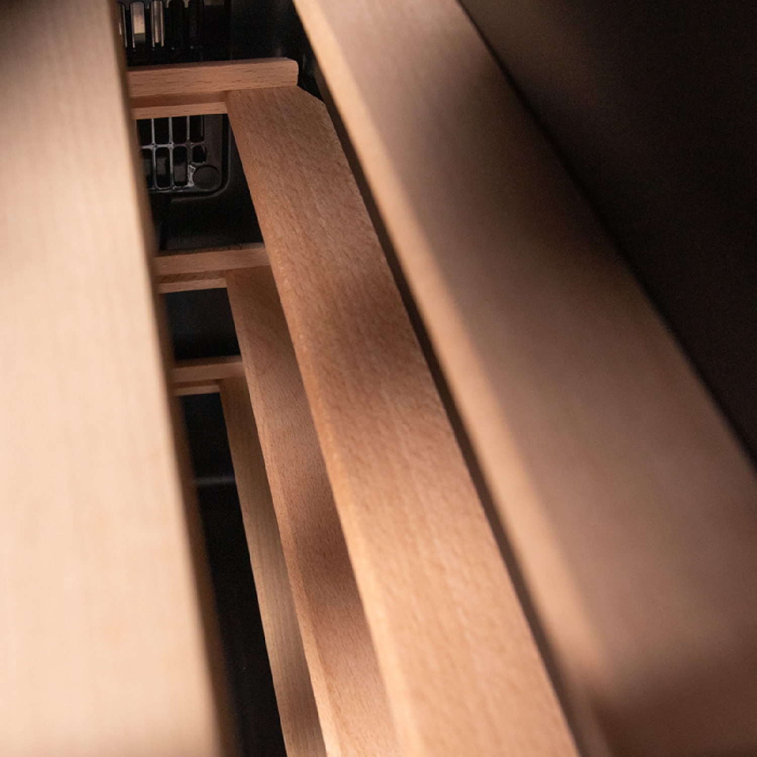 Drewniany stojak na wino z widocznymi listwami i ciemnym wnętrzem. Jasnobrązowe drewno kontrastuje z zacienioną przestrzenią.