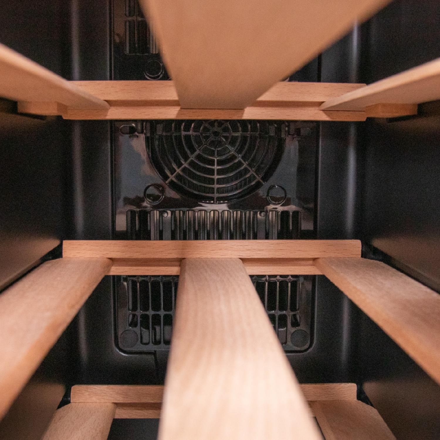 Wnętrze chłodziarki do wina. Drewniane półki na pierwszym planie, czarne wnętrze i wentylator pośrodku.