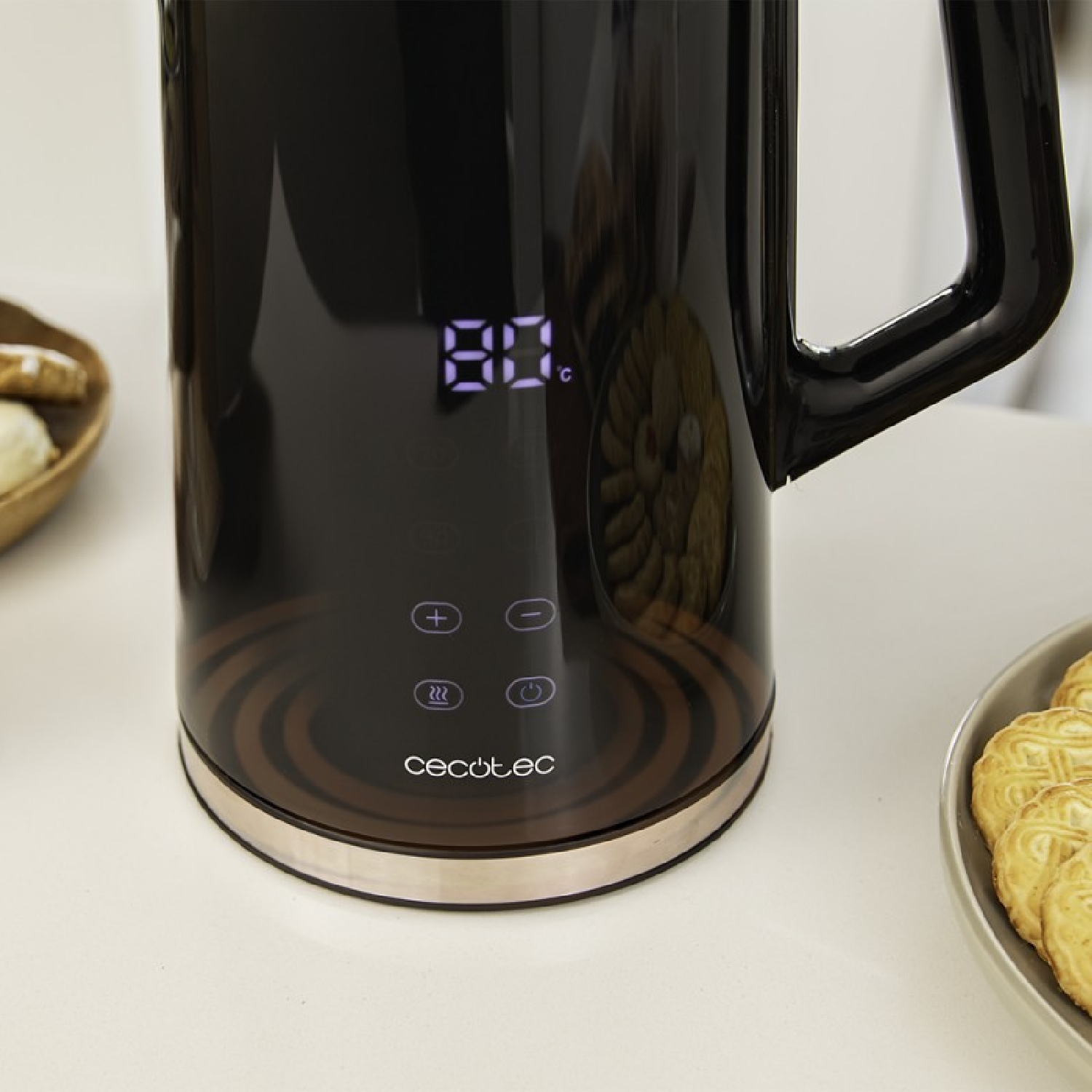 Bollitore elettrico nero con 80°C. Biscotti in una ciotola grigia e ciotola di legno con pasticcini accanto, tutto su superficie bianca.