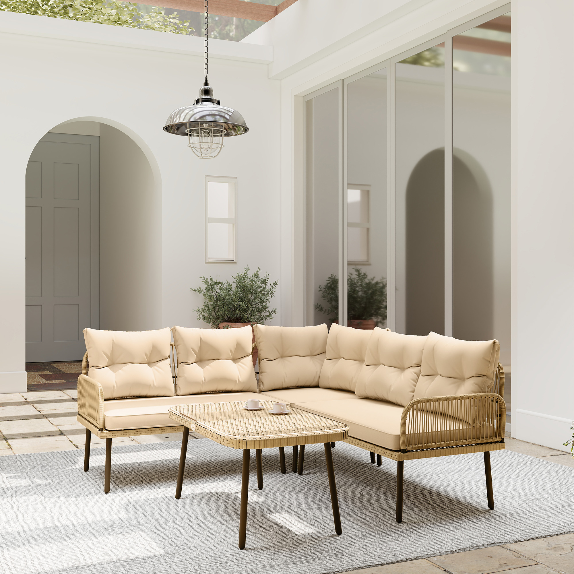 Area salotto all'aperto con cuscini beige, tavolo in vimini e lampada a sospensione. Pareti bianche e grandi porte in vetro.