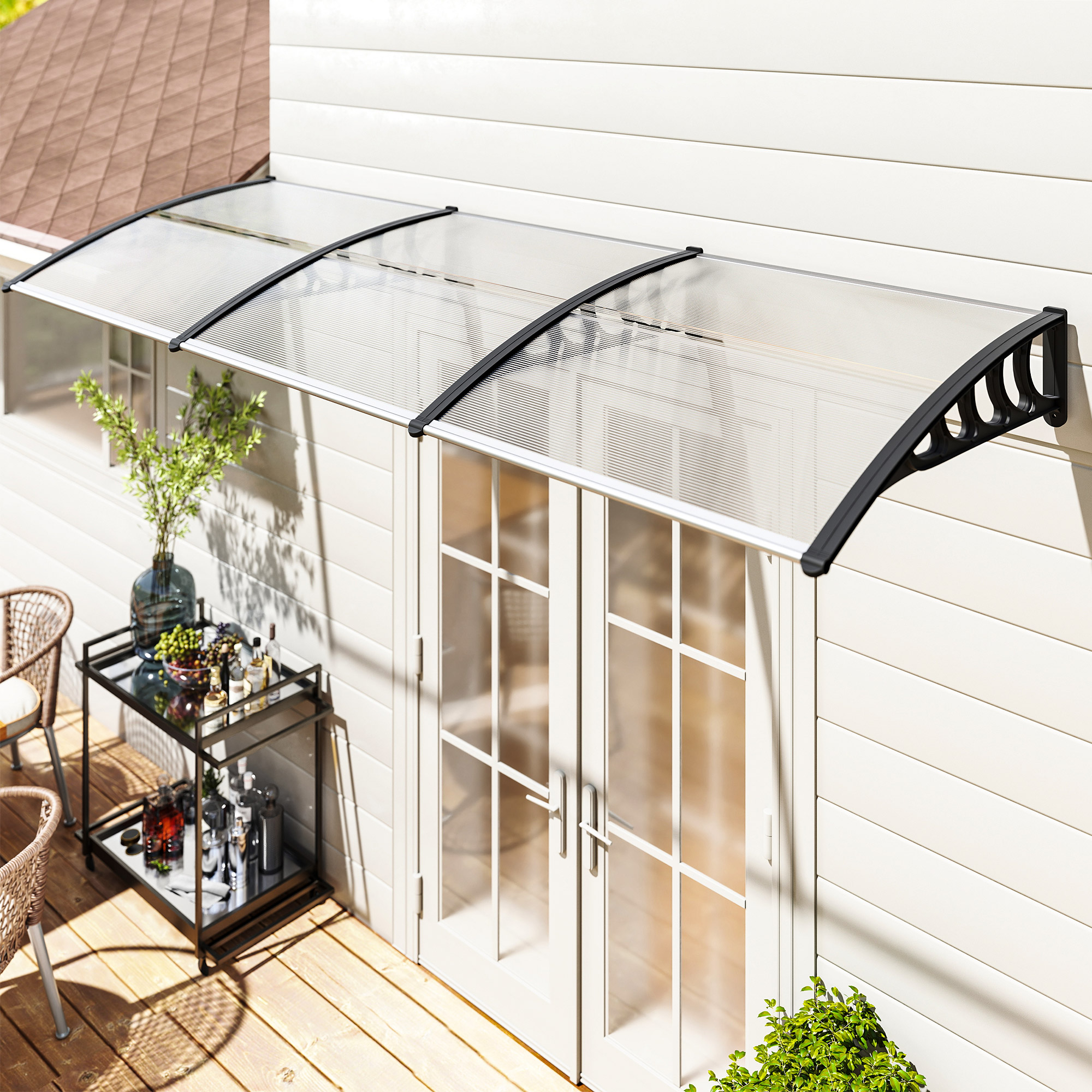 Un toldo transparente sobre puertas francesas blancas. Un carrito de bar con bebidas está en una terraza de madera. Una planta verde a la derecha.