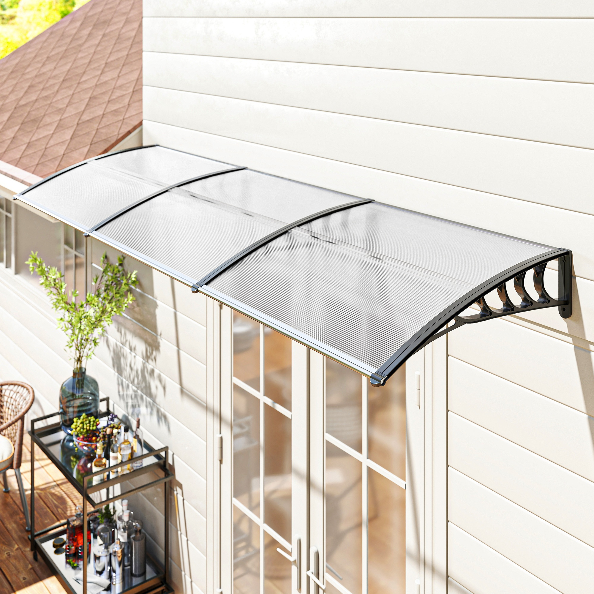 Un toldo transparente sobre una puerta blanca. Un carrito de bar, plantas y una casa al fondo.