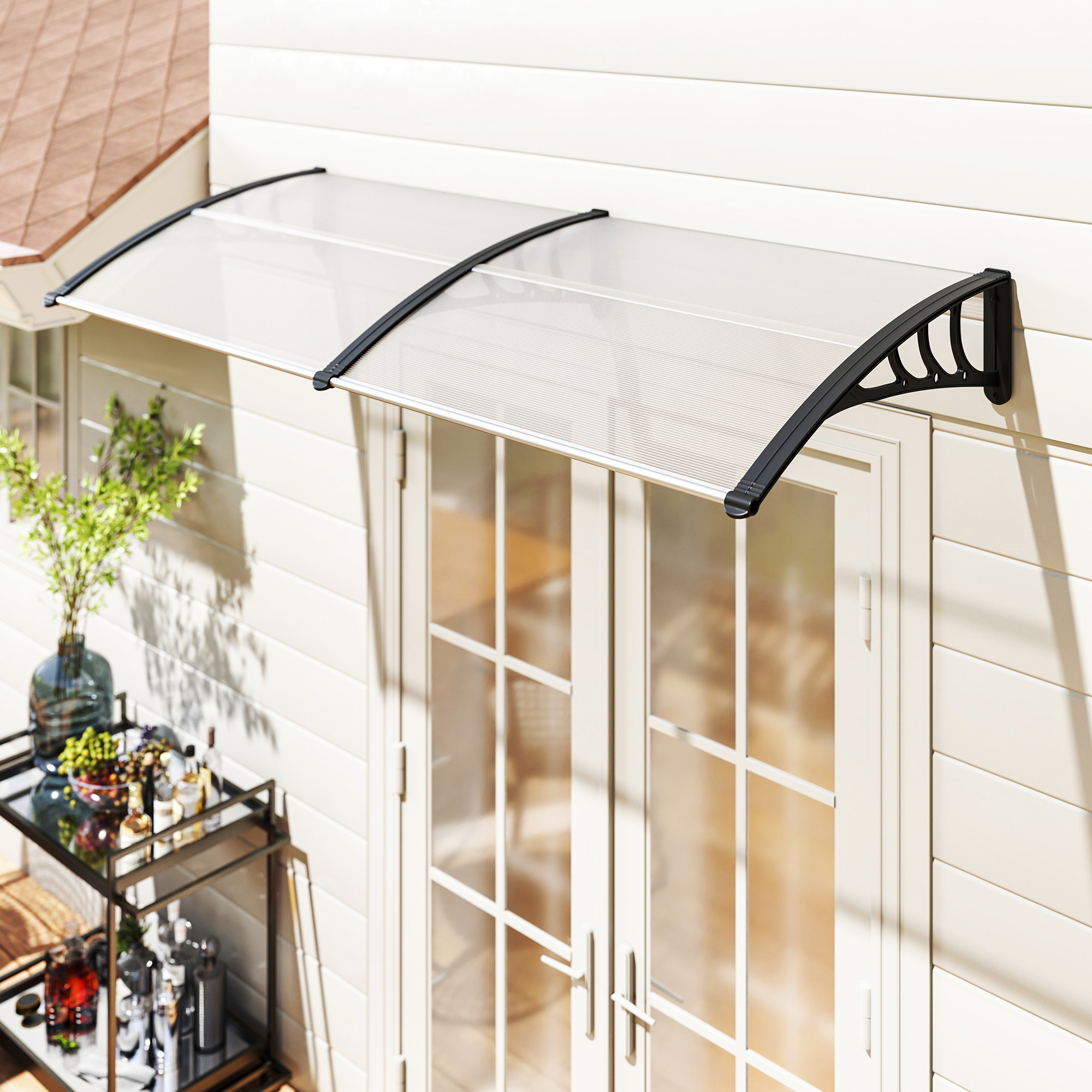 Un toldo transparente sobre puertas francesas blancas. Un carrito de bar con bebidas y un exterior de casa en el fondo.