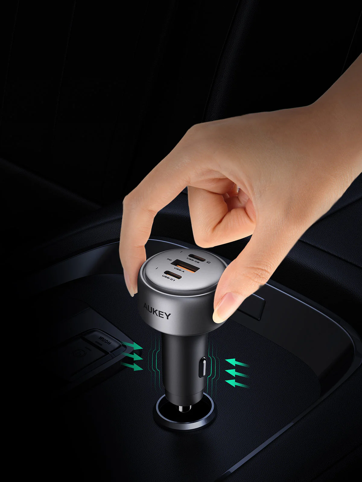Una mano che inserisce un caricabatterie per auto nella presa di corrente dell'auto. Il caricabatterie è argentato, ha porte USB ed è etichettato AUKEY.